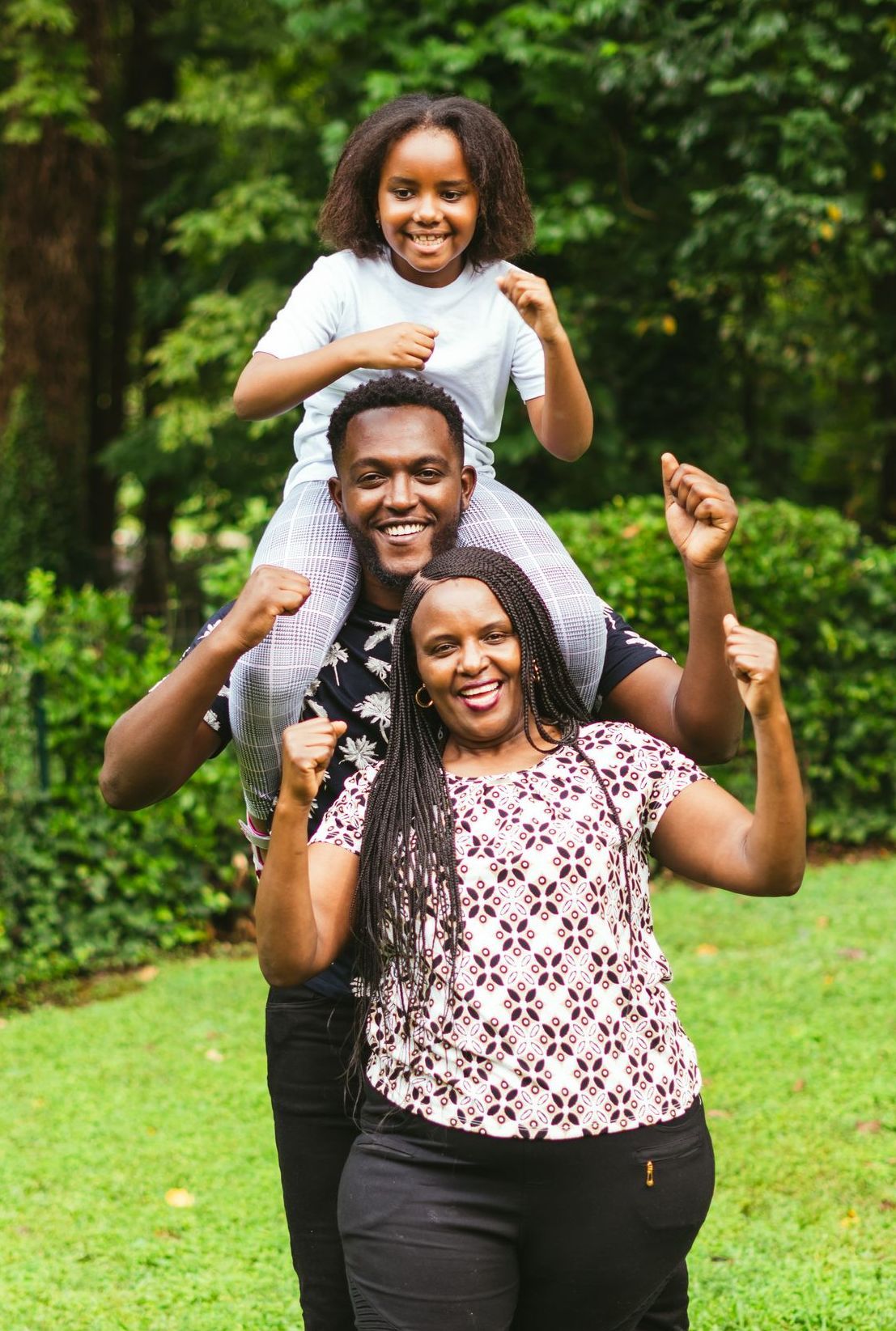 A man is carrying a little girl on his shoulders in a park.