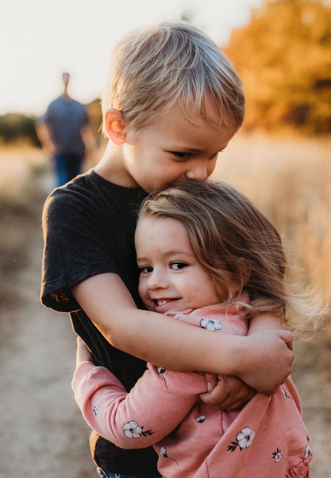 A boy and a girl are hugging each other in a field.