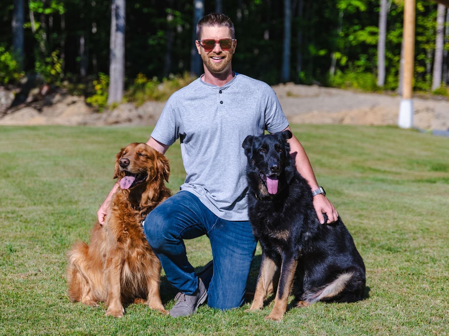 Evan kneeling down with two dogs in the grass.