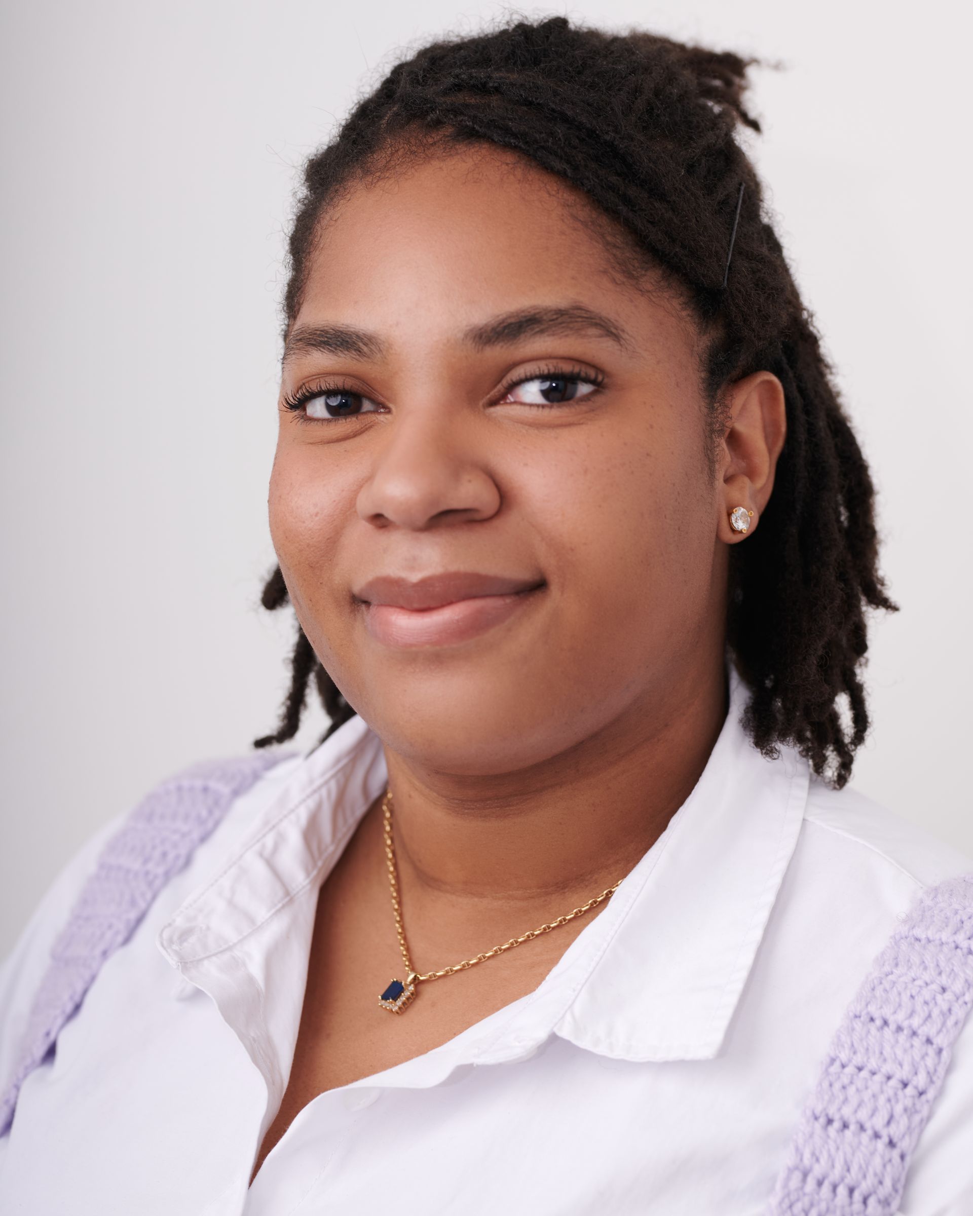 Une femme avec des dreadlocks porte une chemise blanche et un collier en or