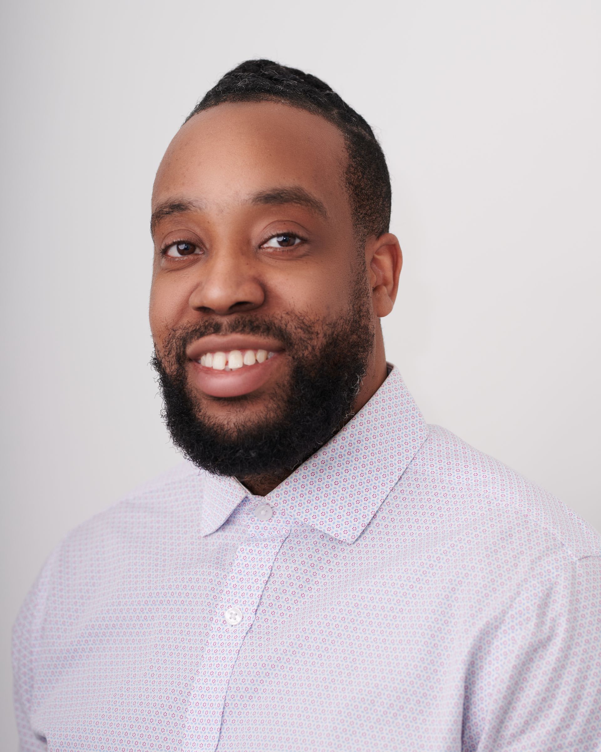 Un homme avec une barbe porte une chemise blanche et sourit à la caméra.