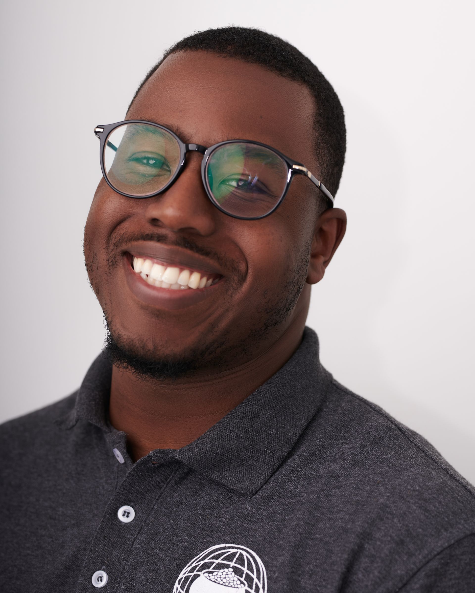 Un homme portant des lunettes et un polo sourit à la caméra.