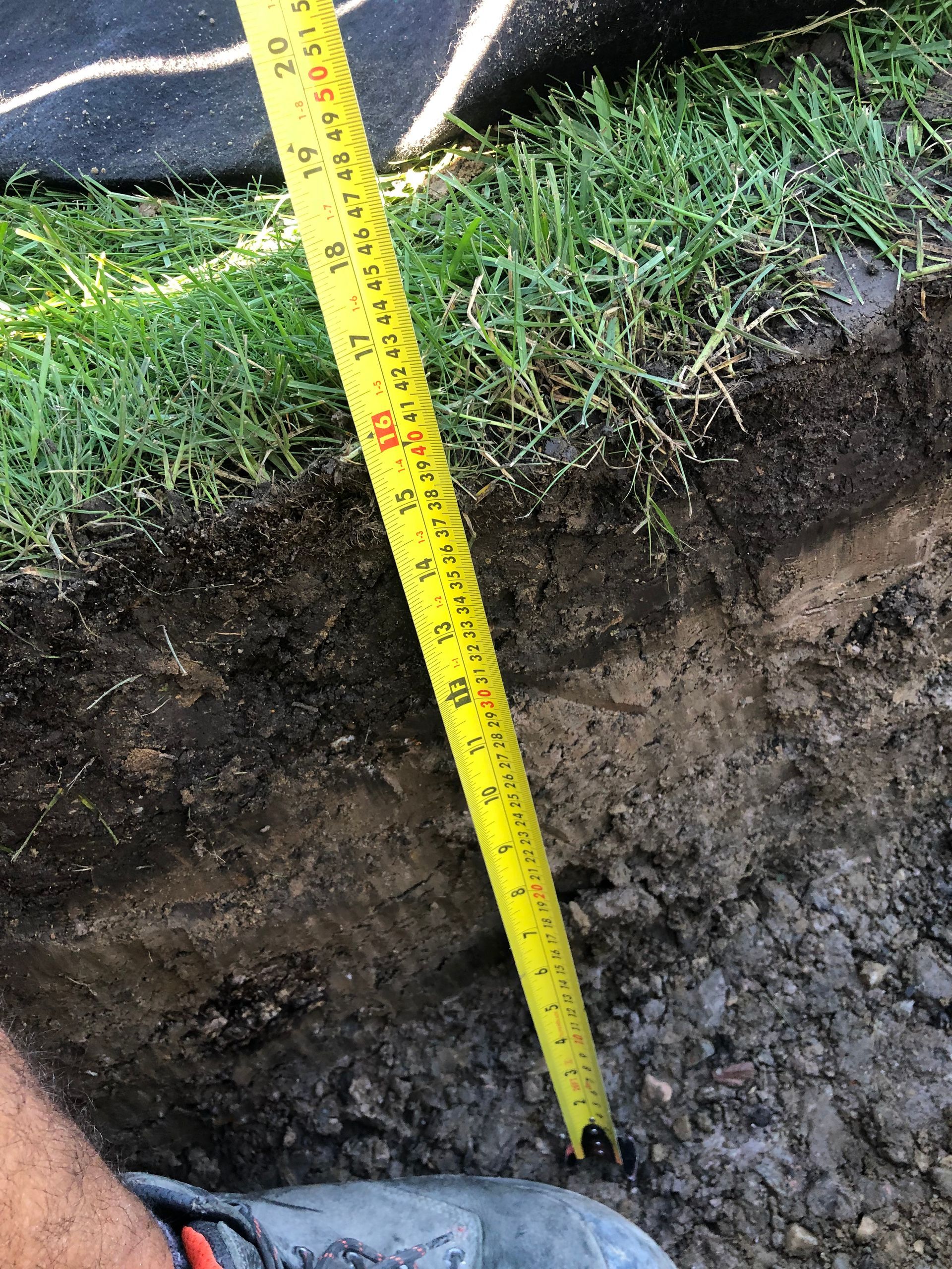 A person is measuring a hole in the ground with a tape measure.