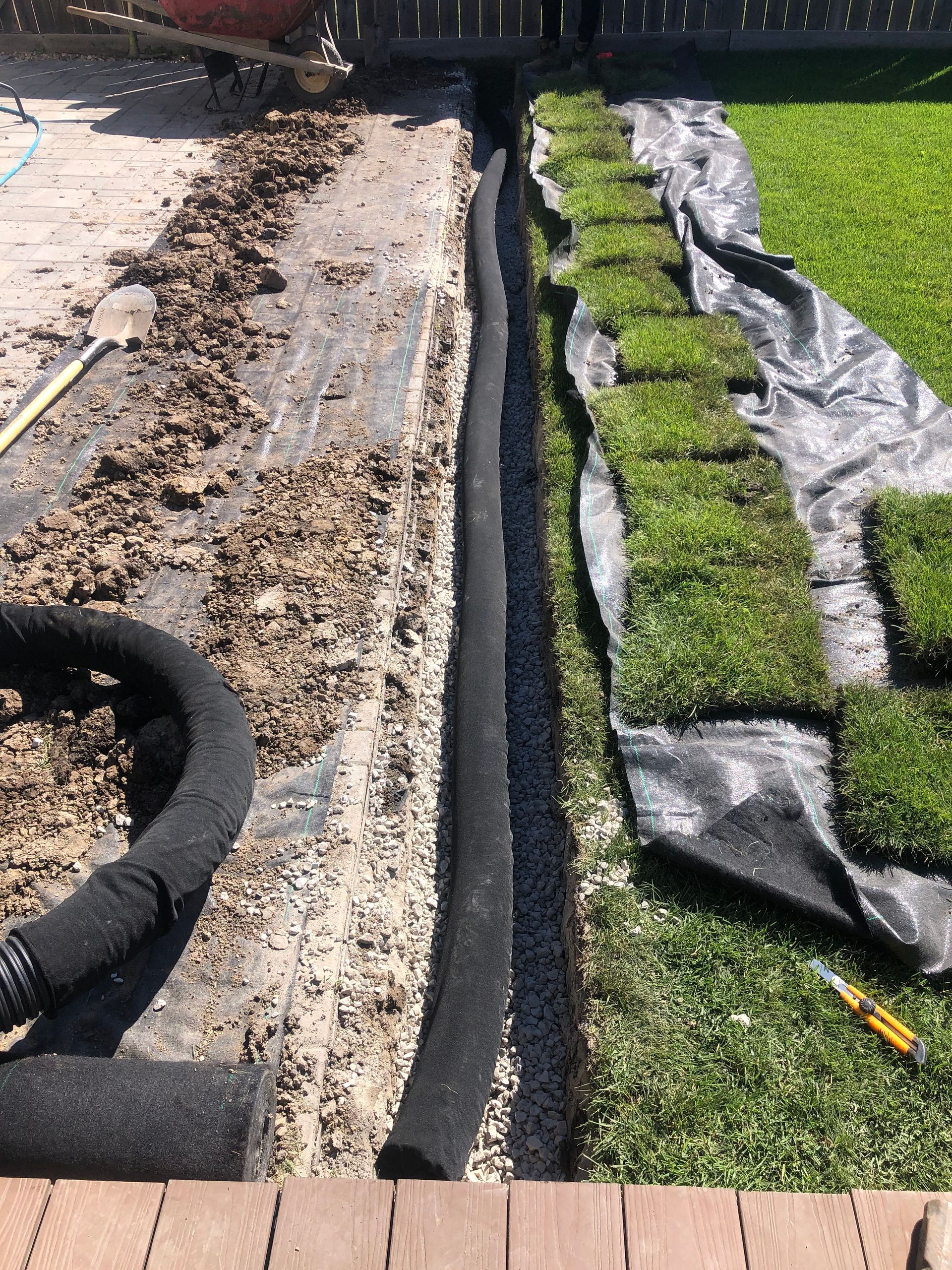 A drain pipe is being installed in a yard next to a lawn.
