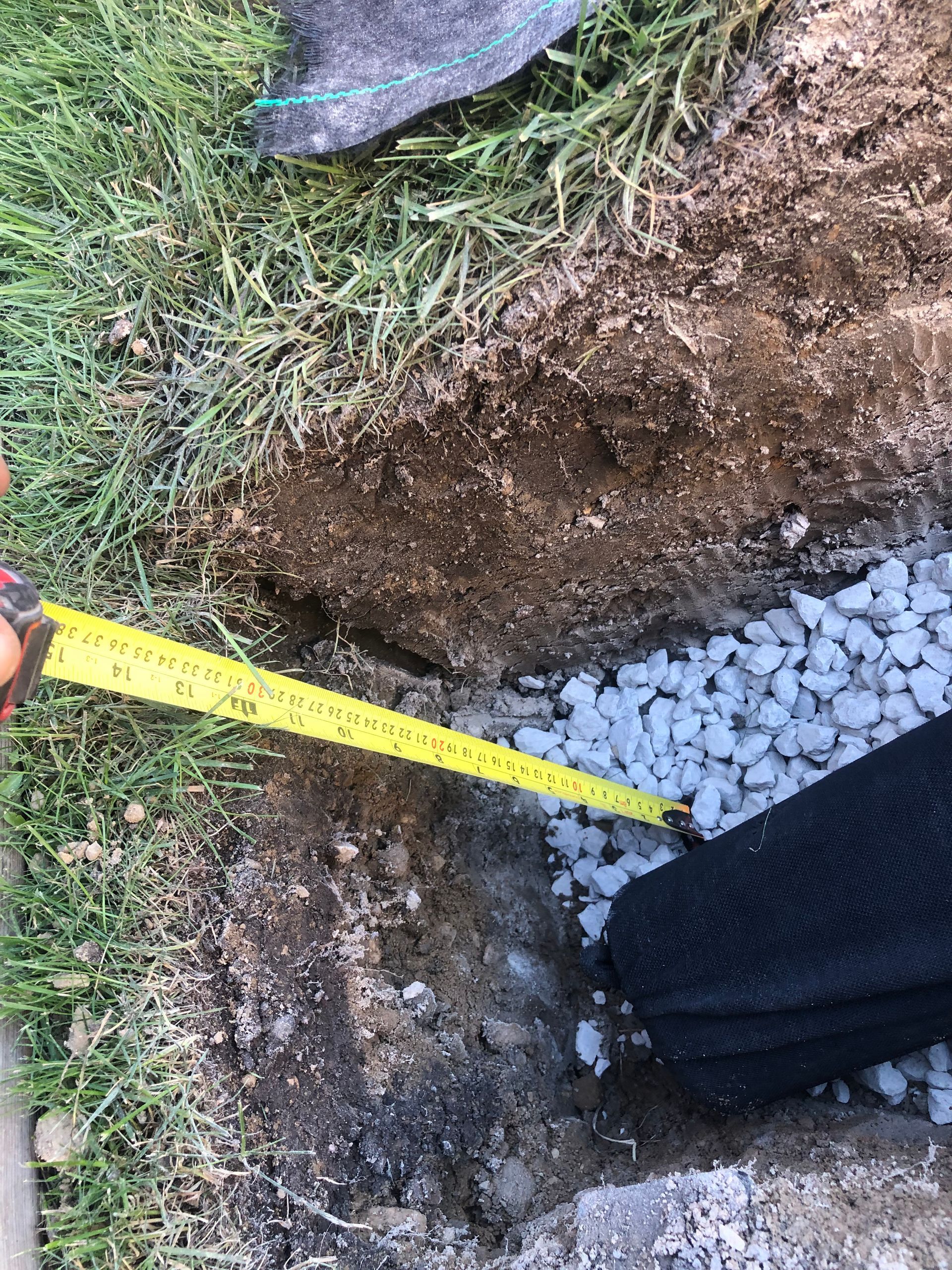 A person is measuring a hole in the ground with a tape measure.