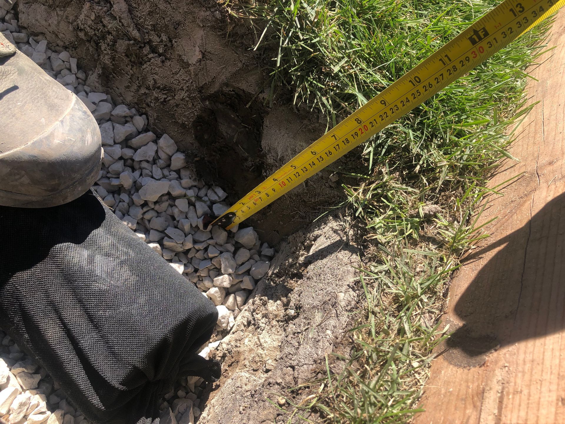 A person is measuring a hole in the ground with a tape measure.