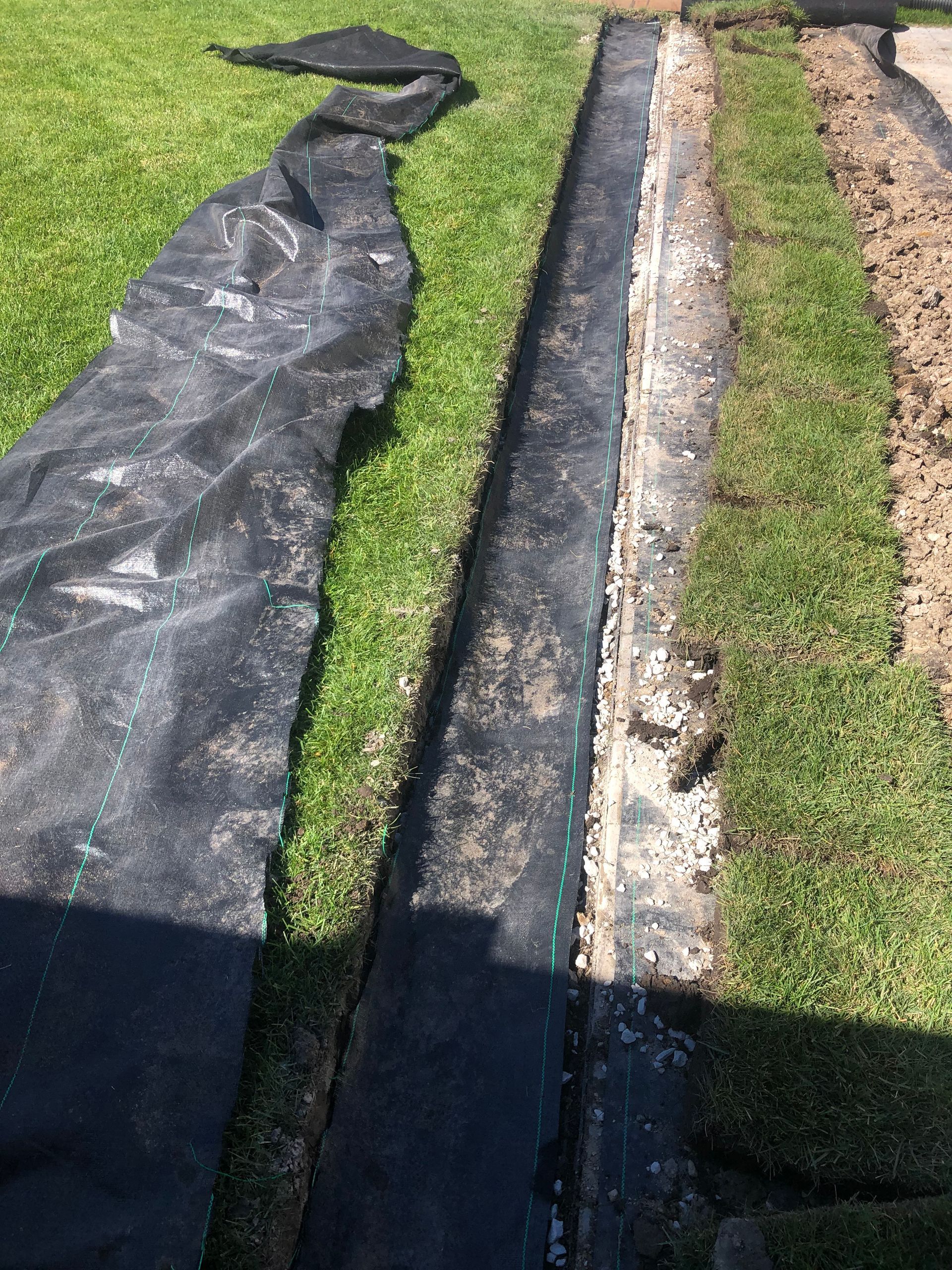 A black tarp is laying on the grass next to a concrete curb.