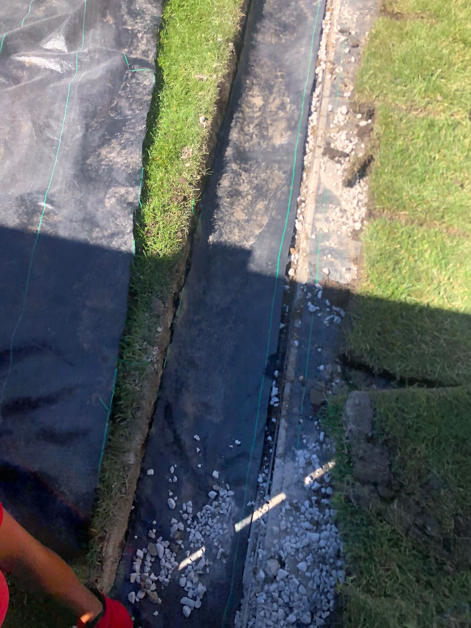 A person is standing next to a drain in a yard.