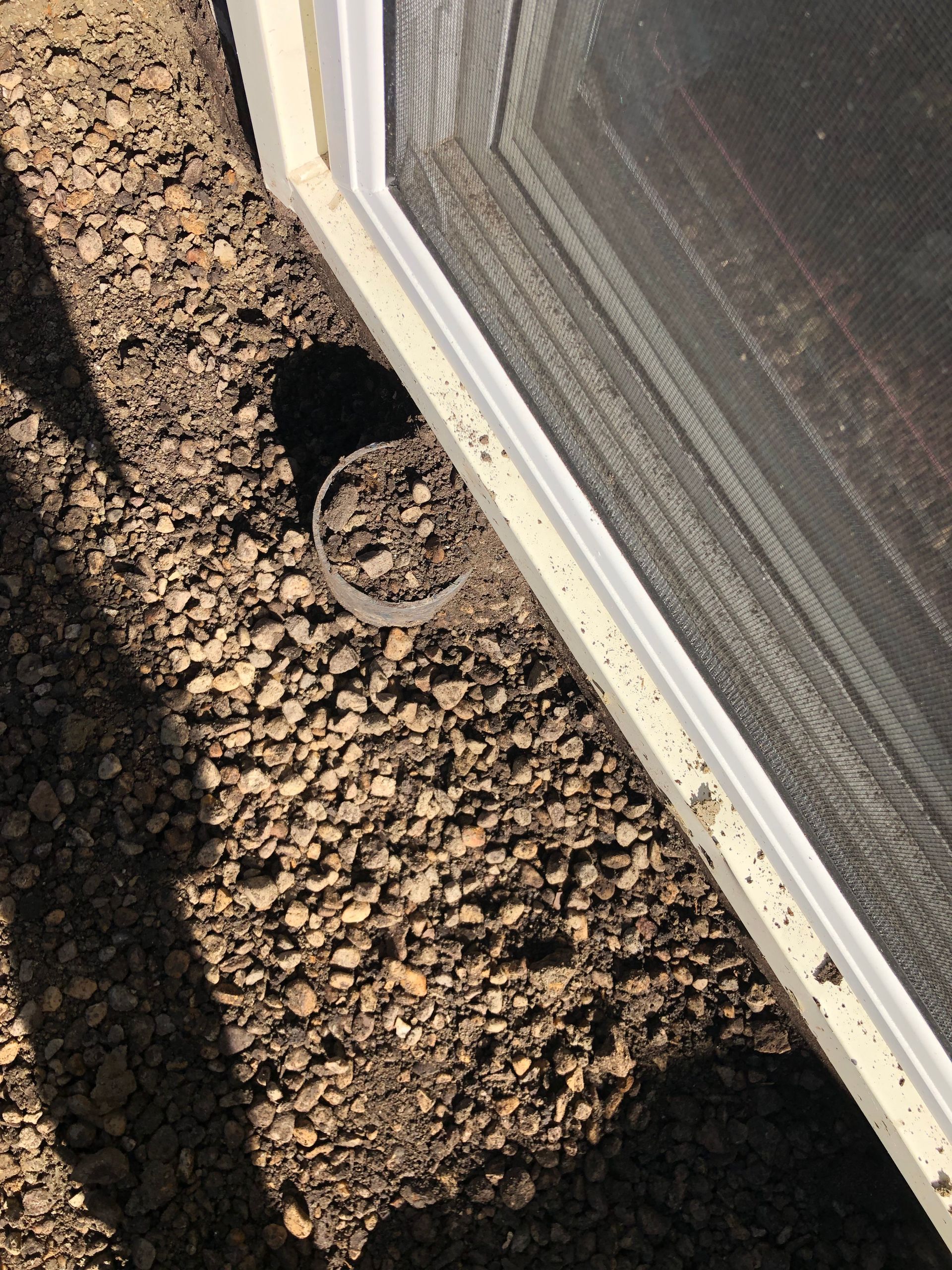 A sliding screen door is sitting on a pile of gravel.