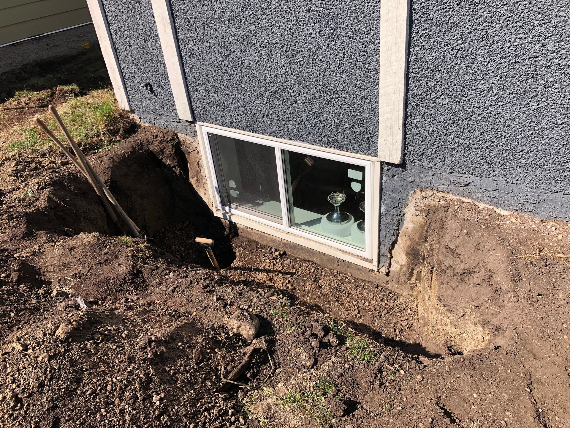 A window is being installed in the basement of a house.