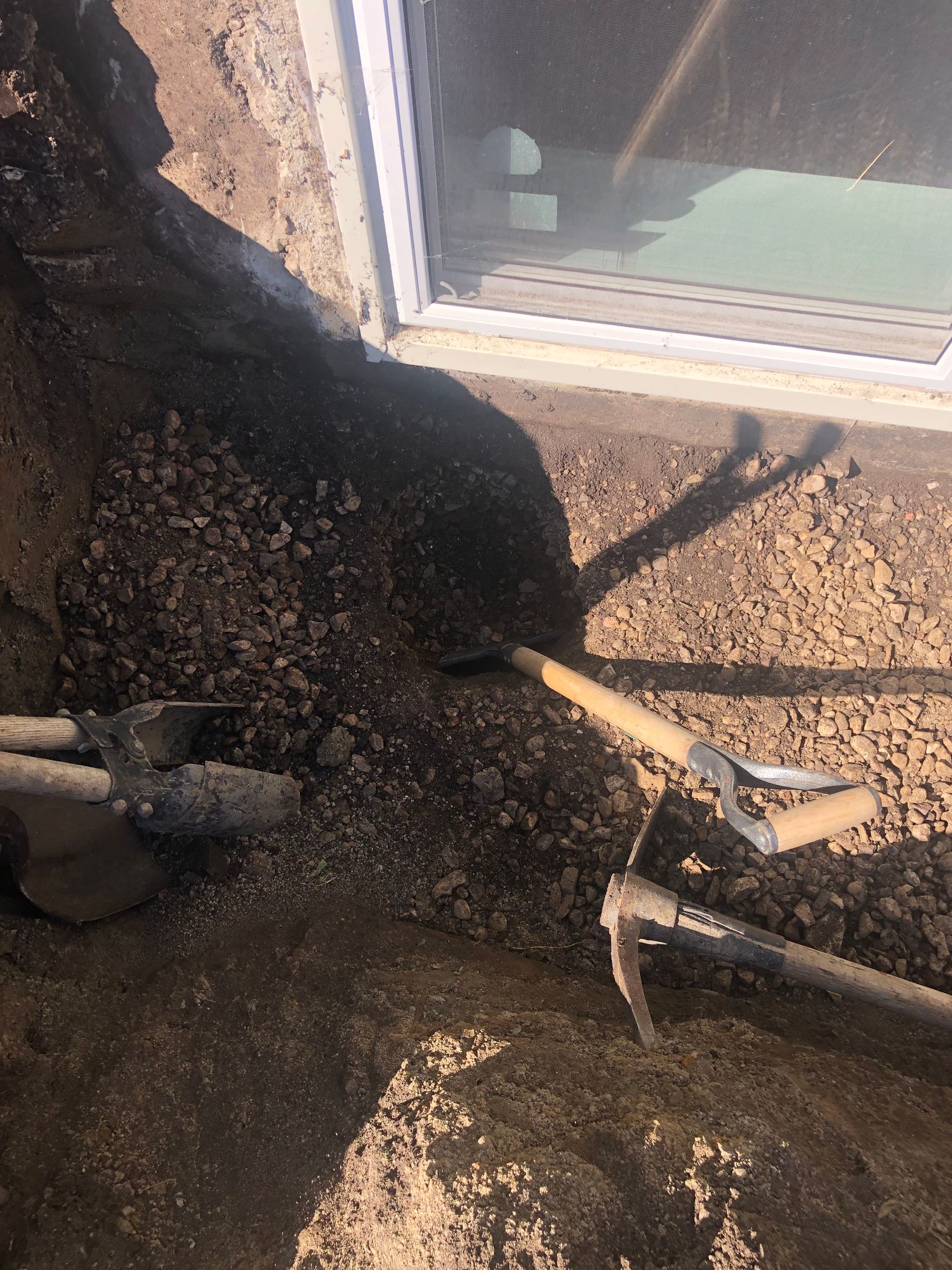 A shovel is sitting on top of a pile of dirt next to a window.
