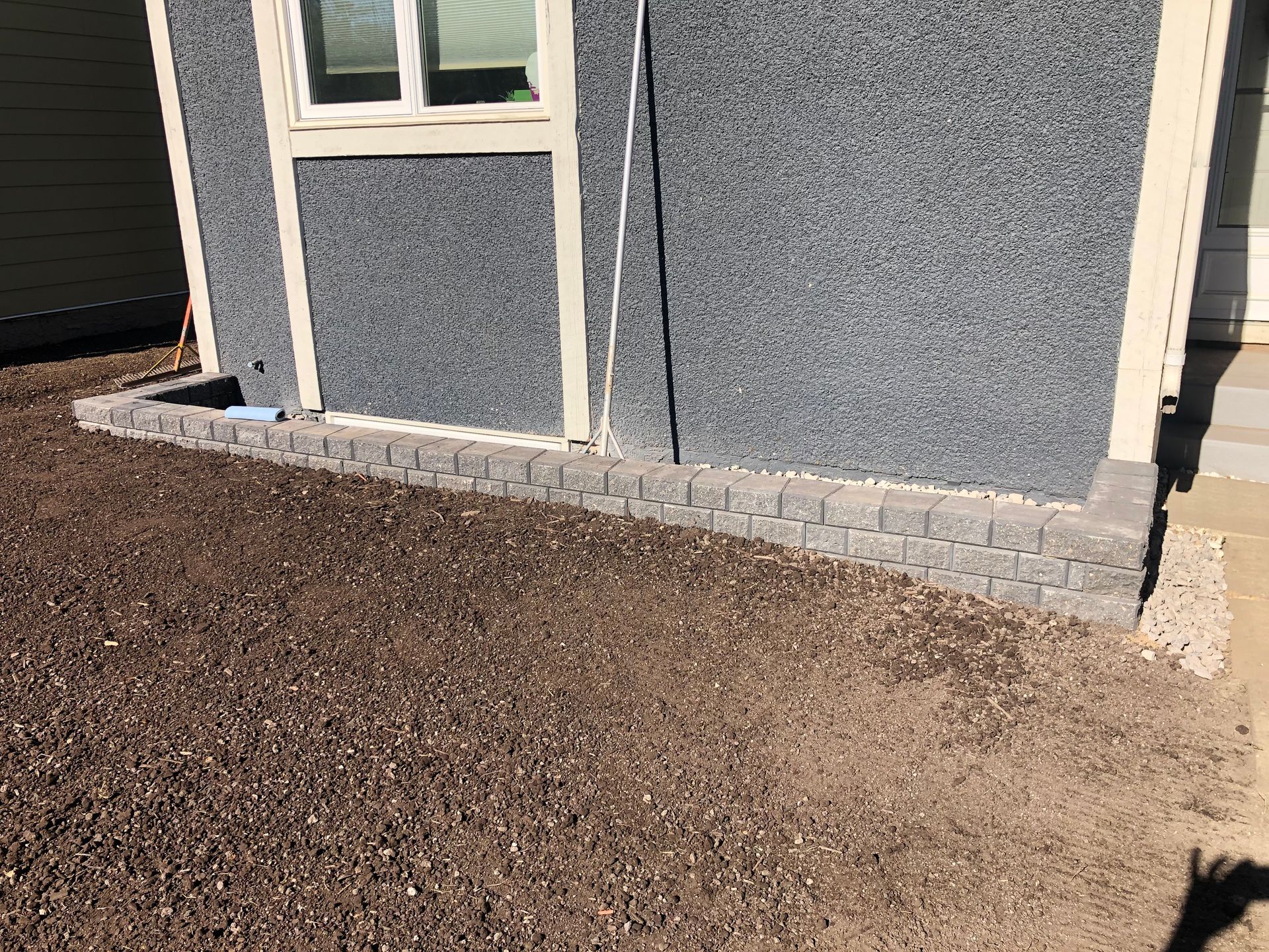 A gray building with a window and a brick walkway in front of it.