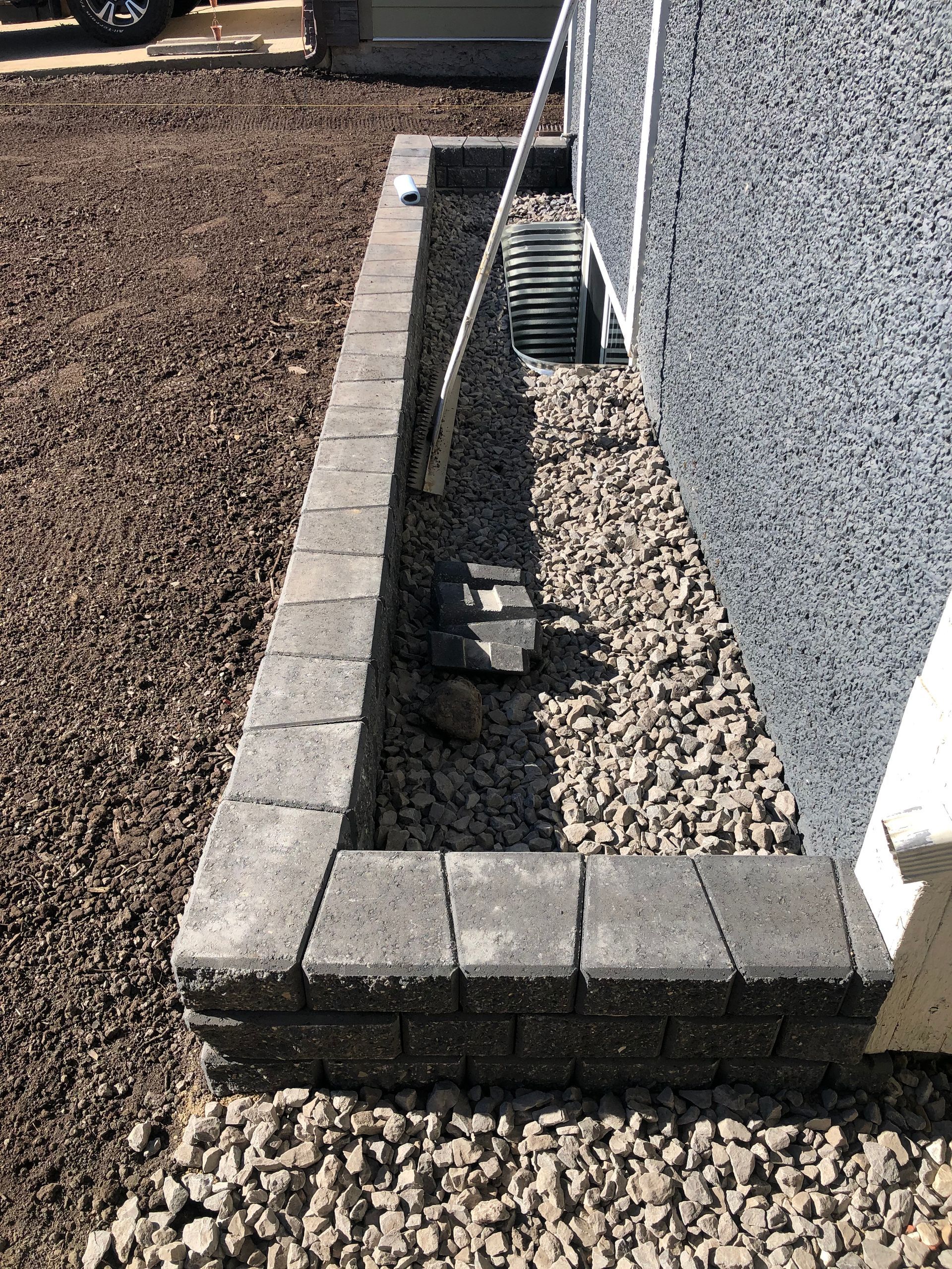A brick wall is surrounded by gravel in front of a house.