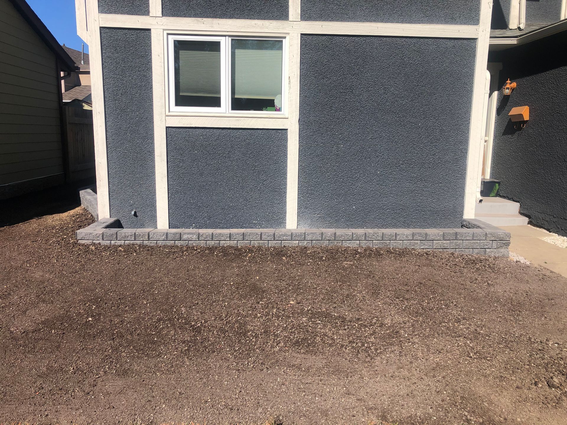 A house with a window on the side of it and gravel in front of it.