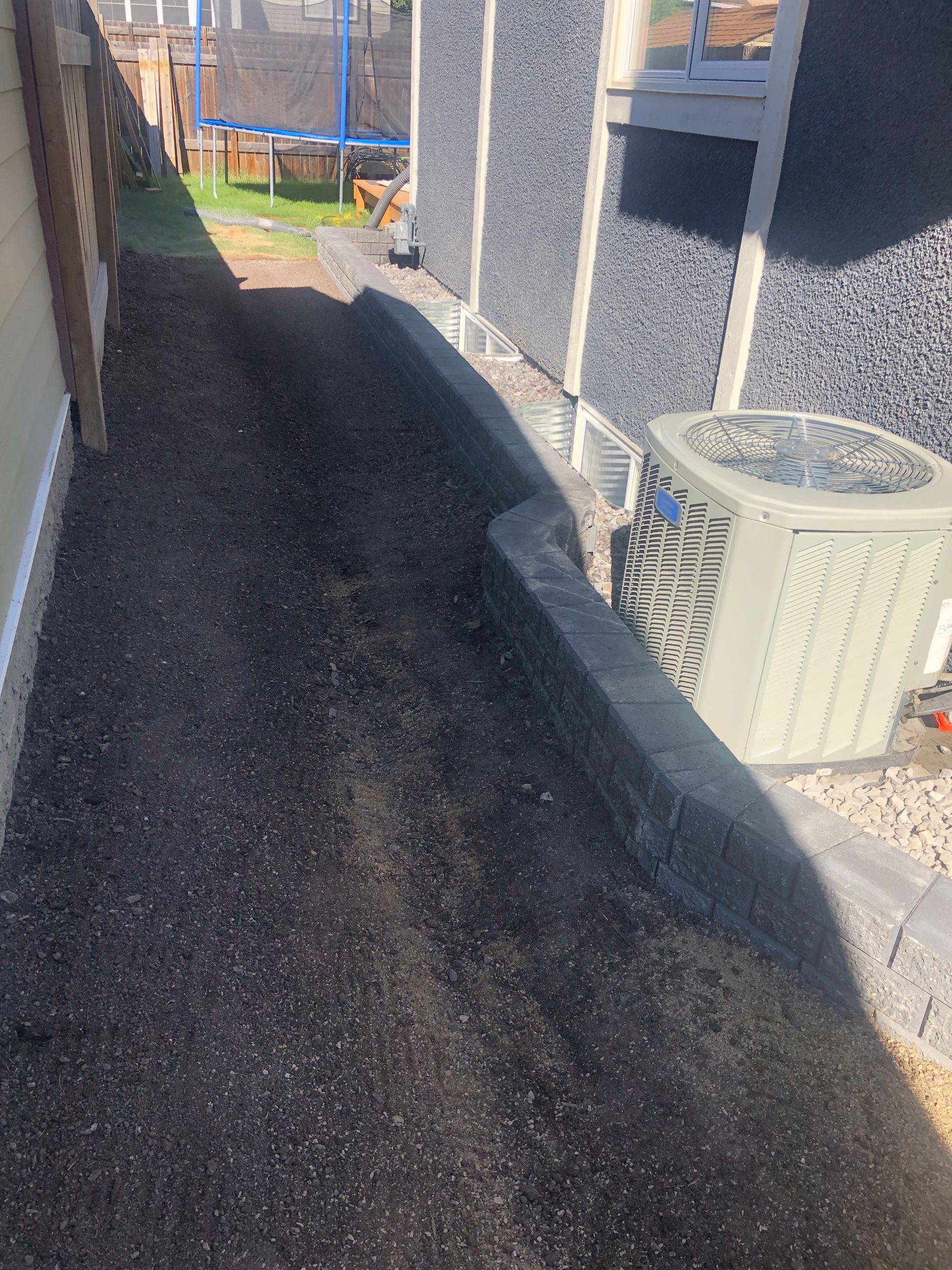 A sidewalk next to a house with a trampoline and an air conditioner.