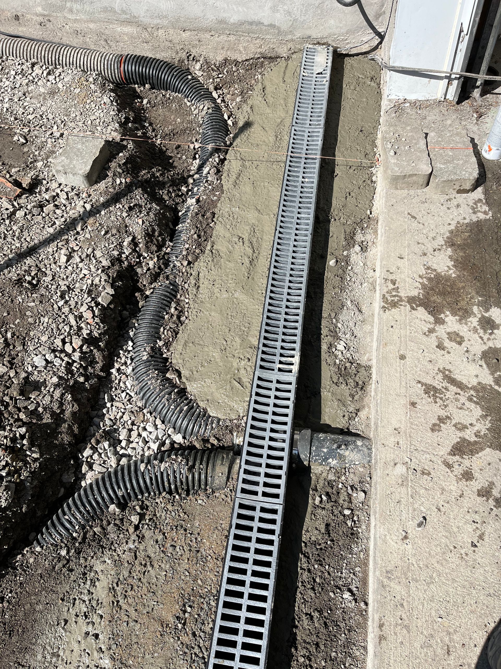 A metal drain is sitting in the dirt next to a concrete wall.