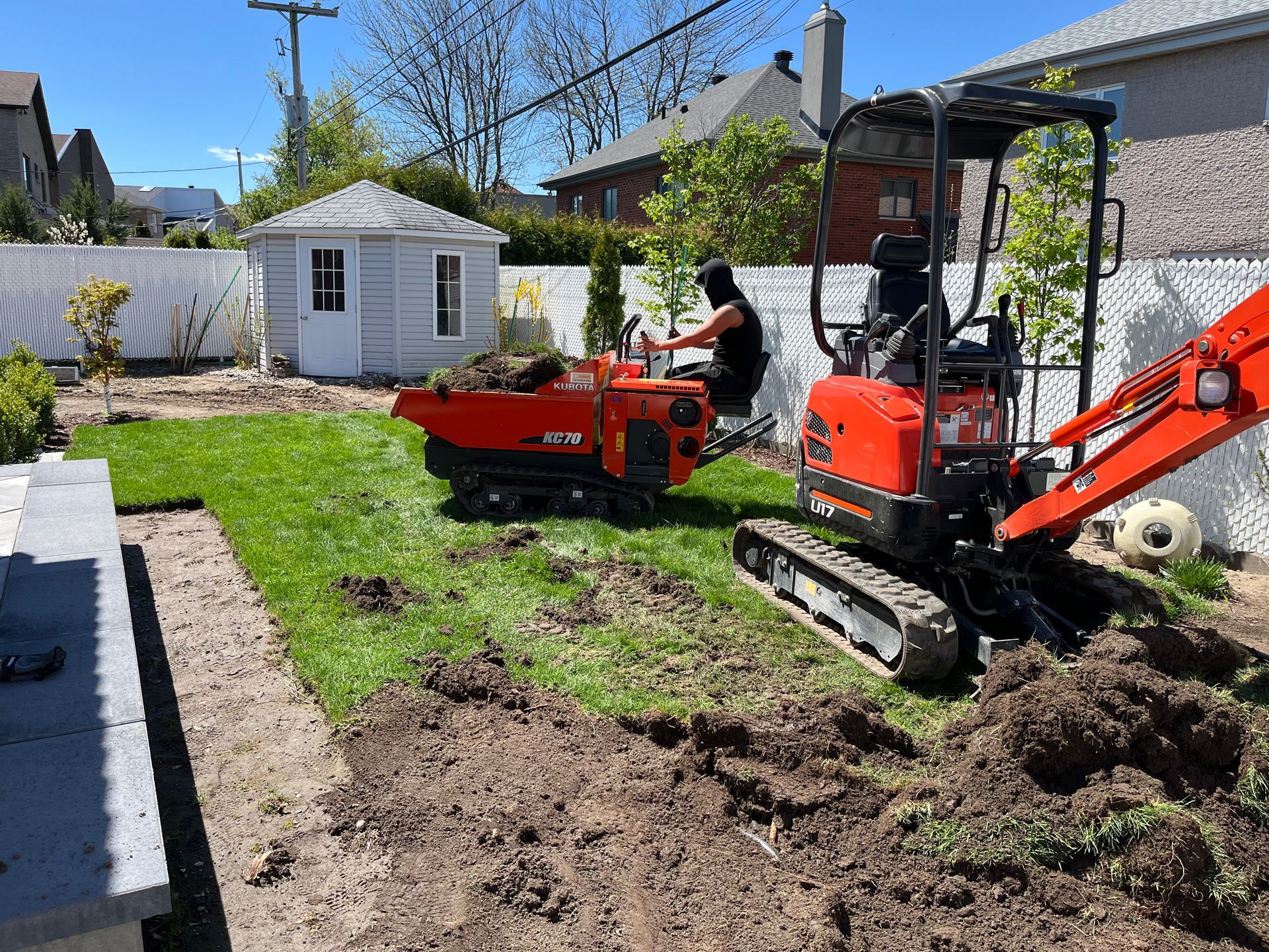 A man is driving a small excavator in a backyard.