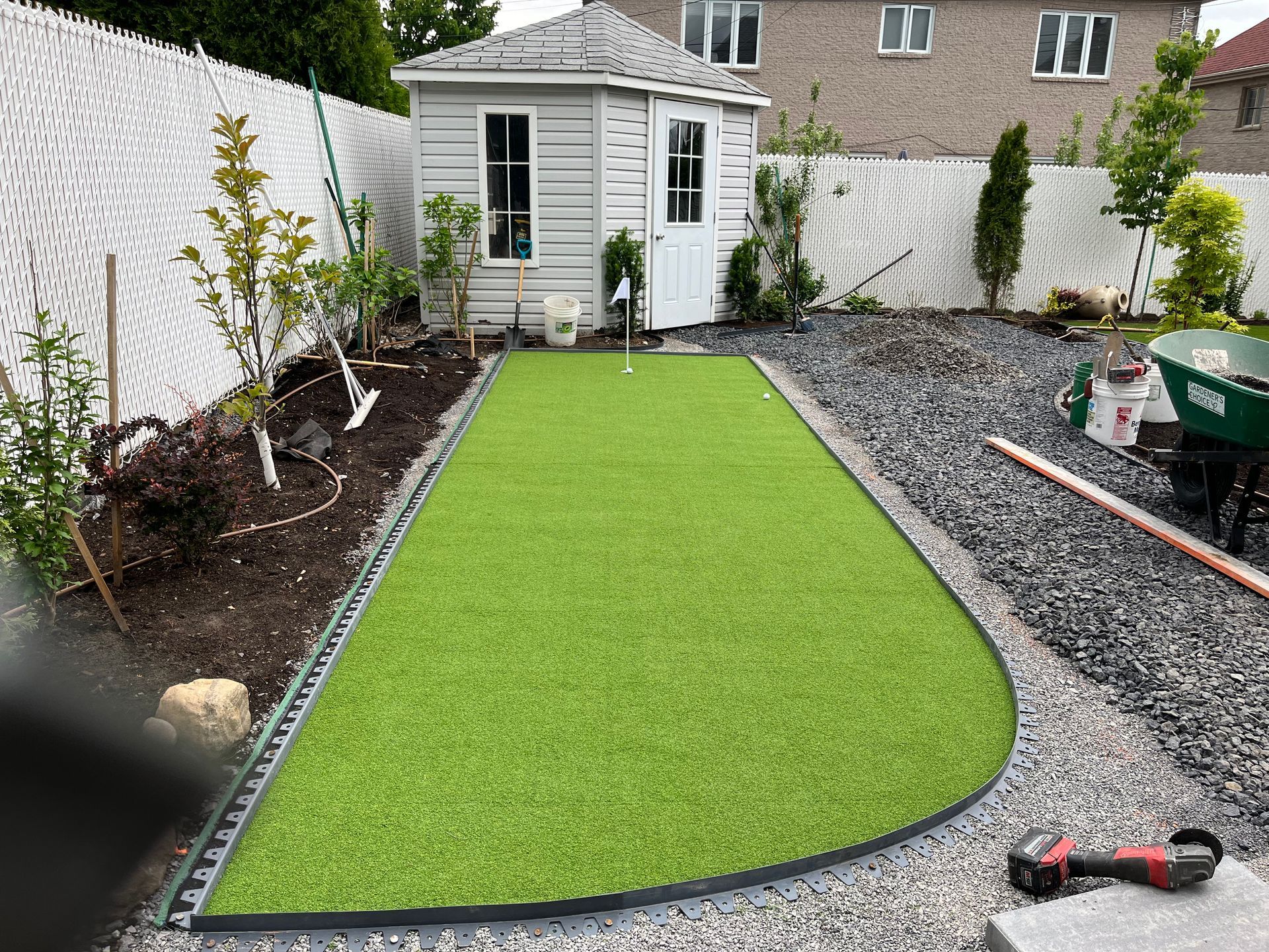 A backyard with a putting green and a shed in the background.