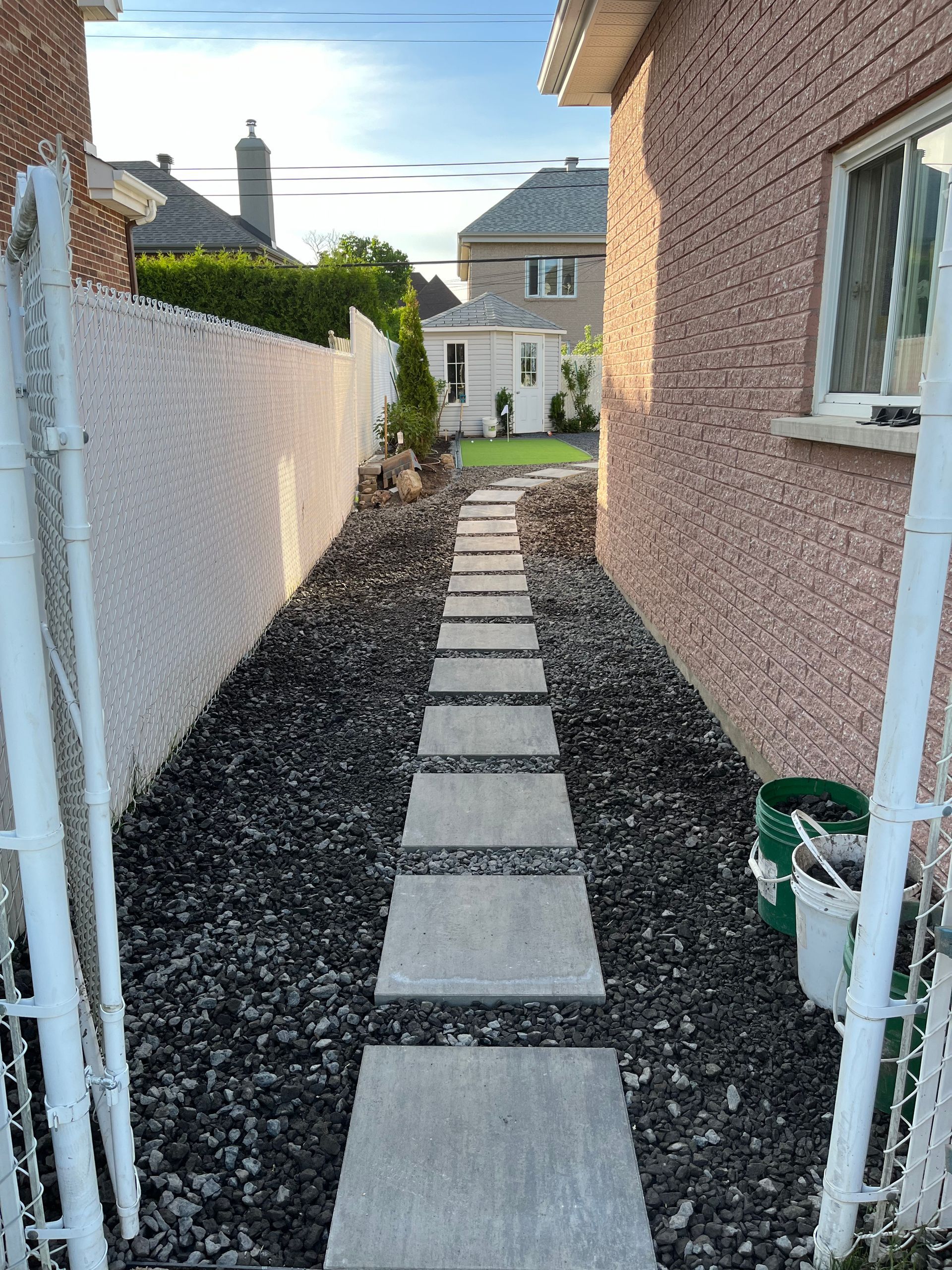 A walkway leading to a house with a brick wall and a white fence.