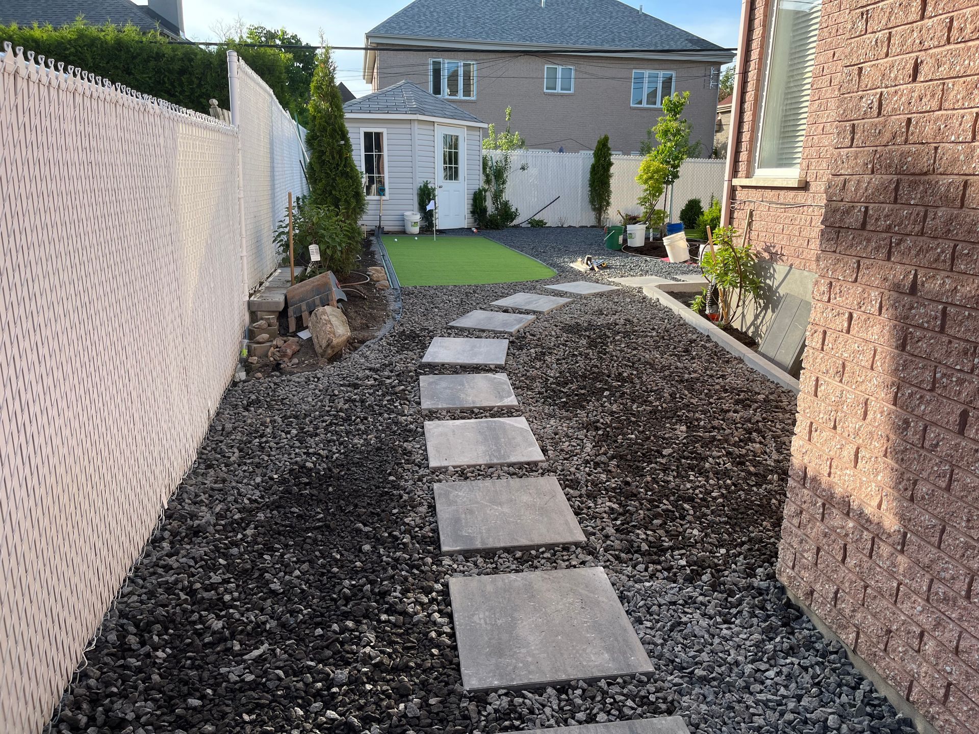 A stone walkway leading to a house with a fence in the background