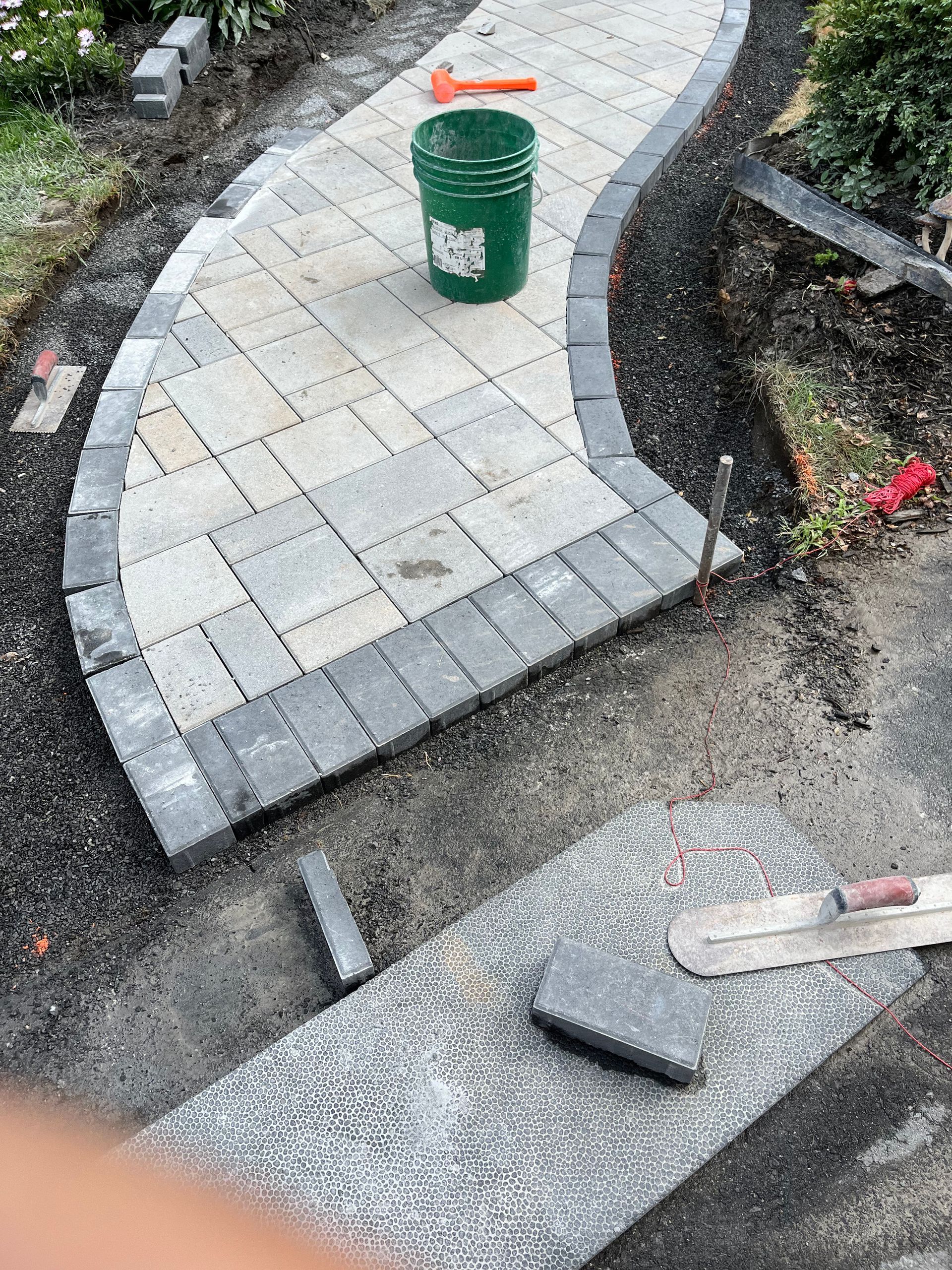 A walkway is being built with bricks and a green bucket.