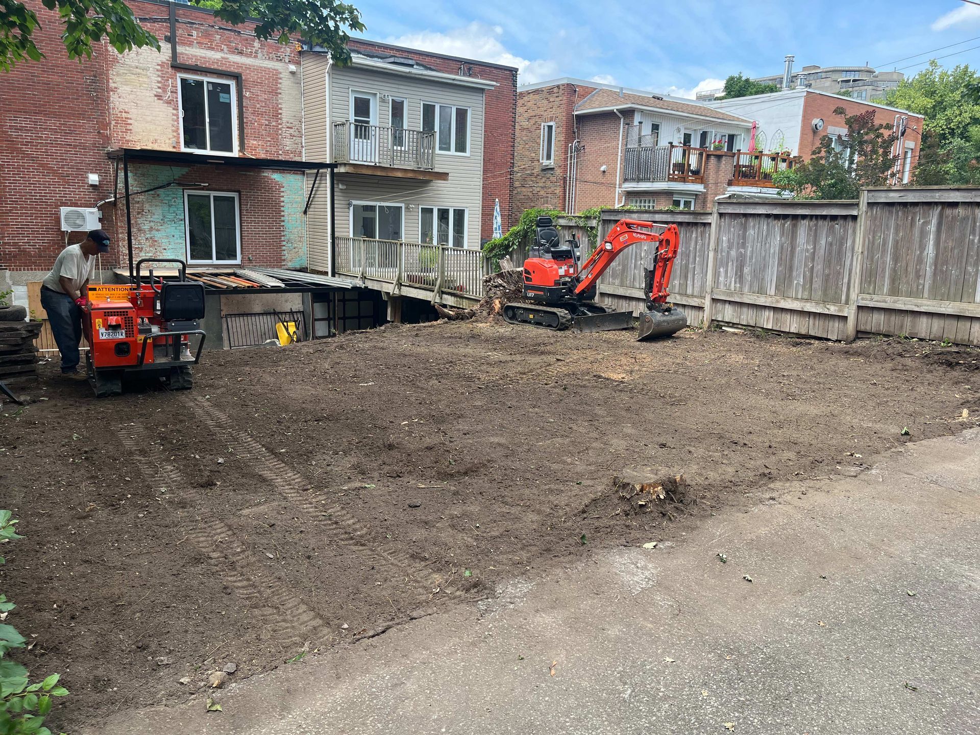 A man is digging a hole in a dirt field in front of a brick building.
