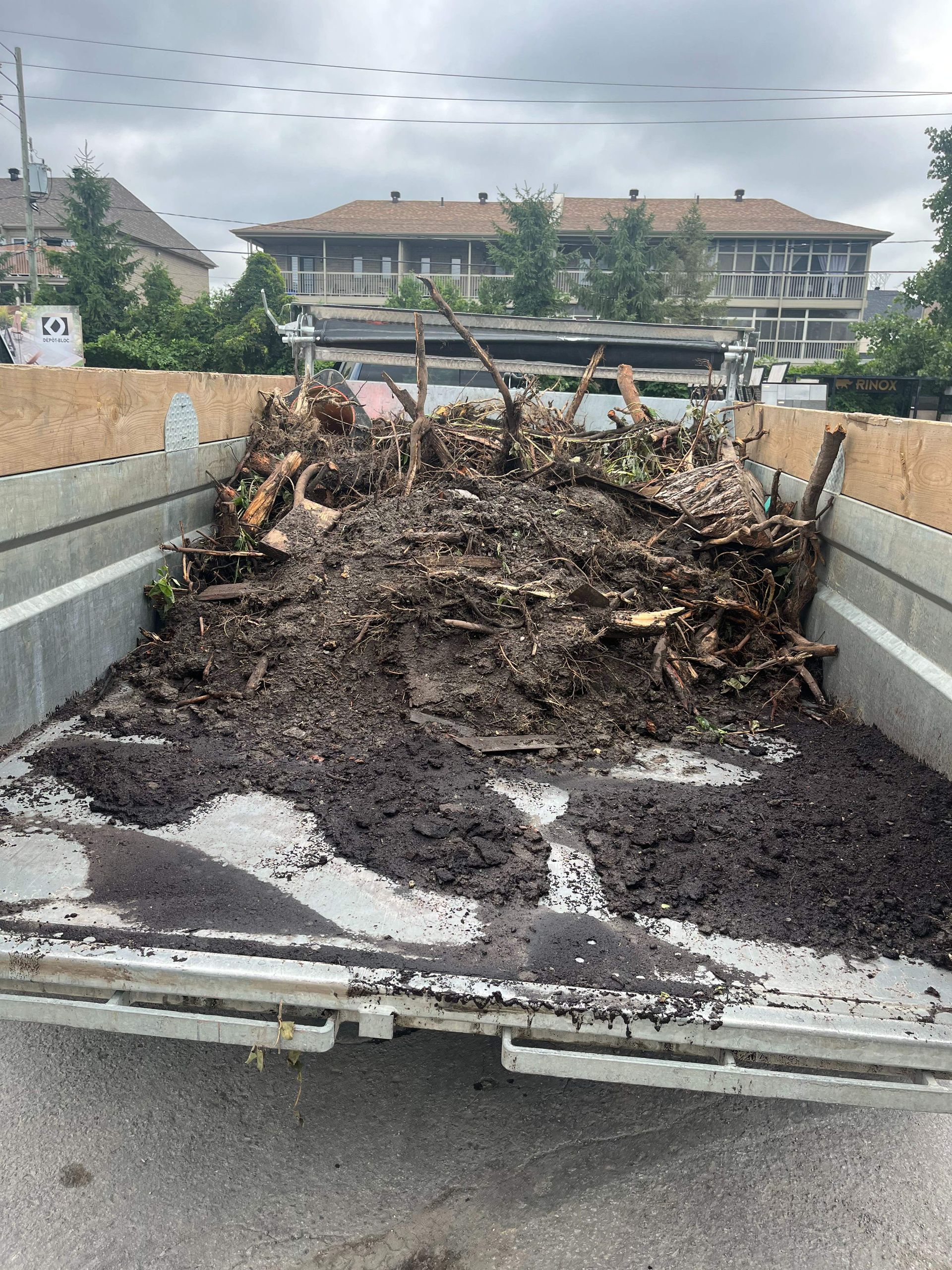 A truck filled with dirt and branches is parked on the side of the road.