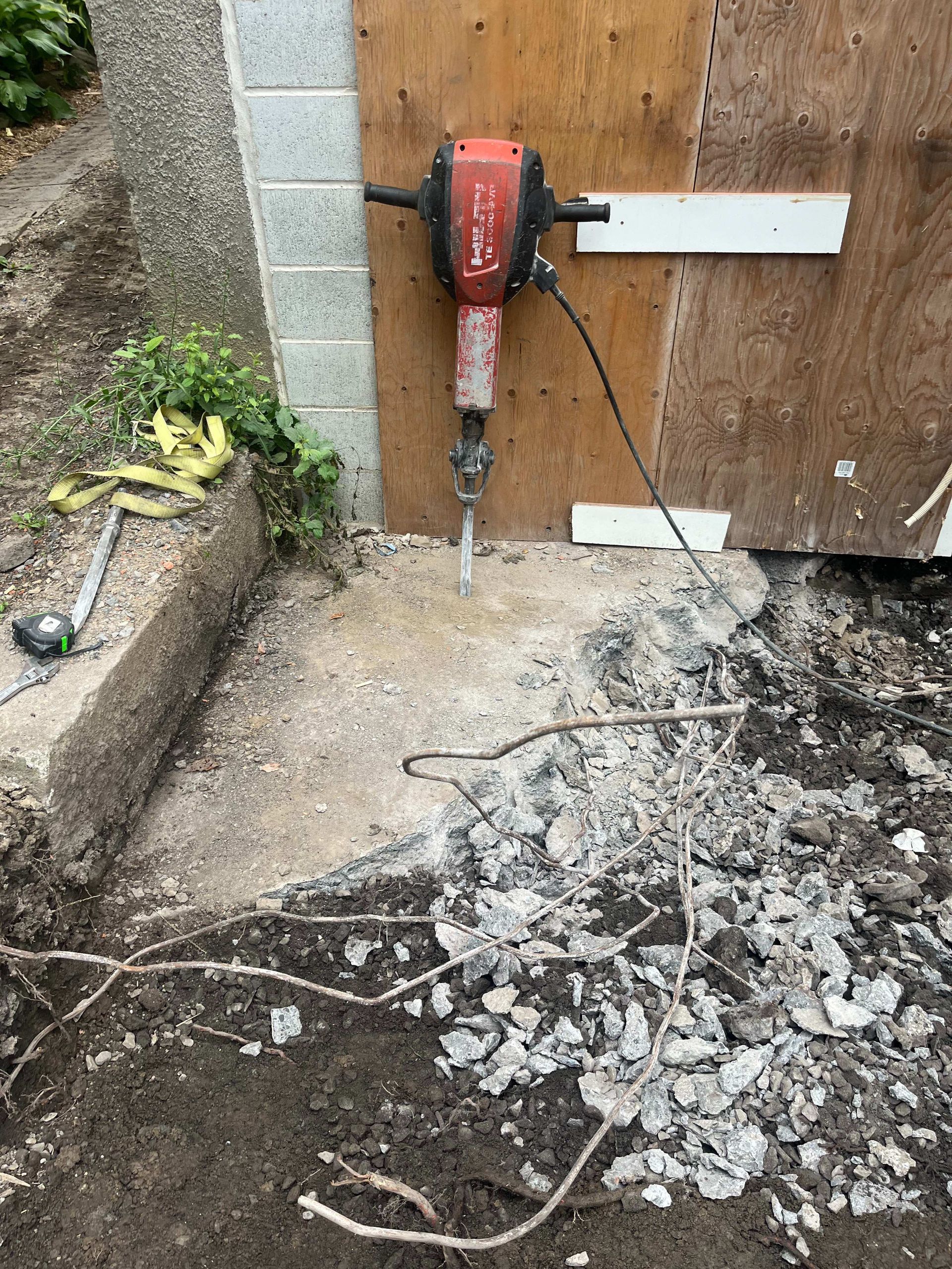 A concrete breaker is sitting on the ground next to a wall.