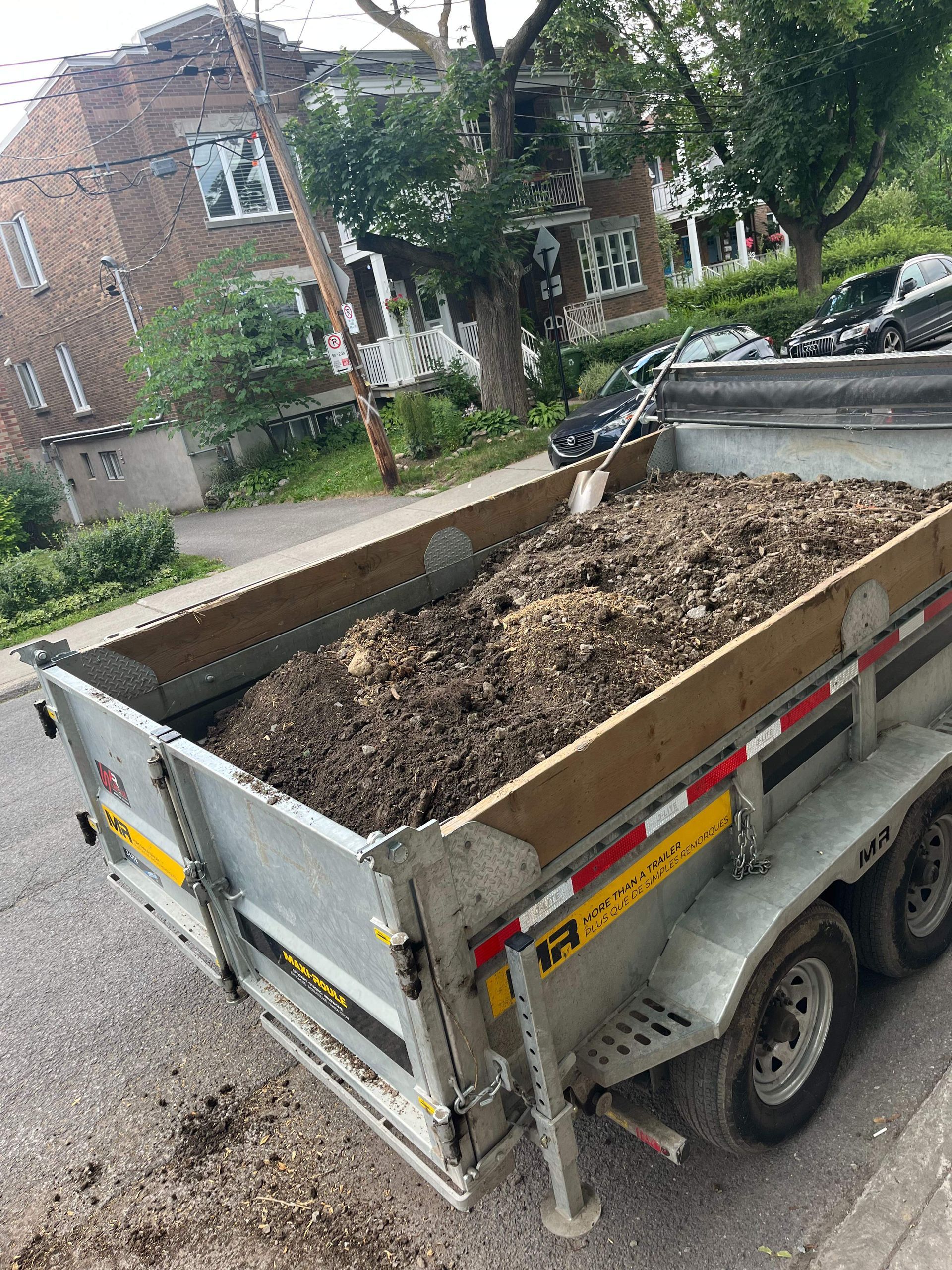 A dump trailer filled with dirt is parked on the side of the road.