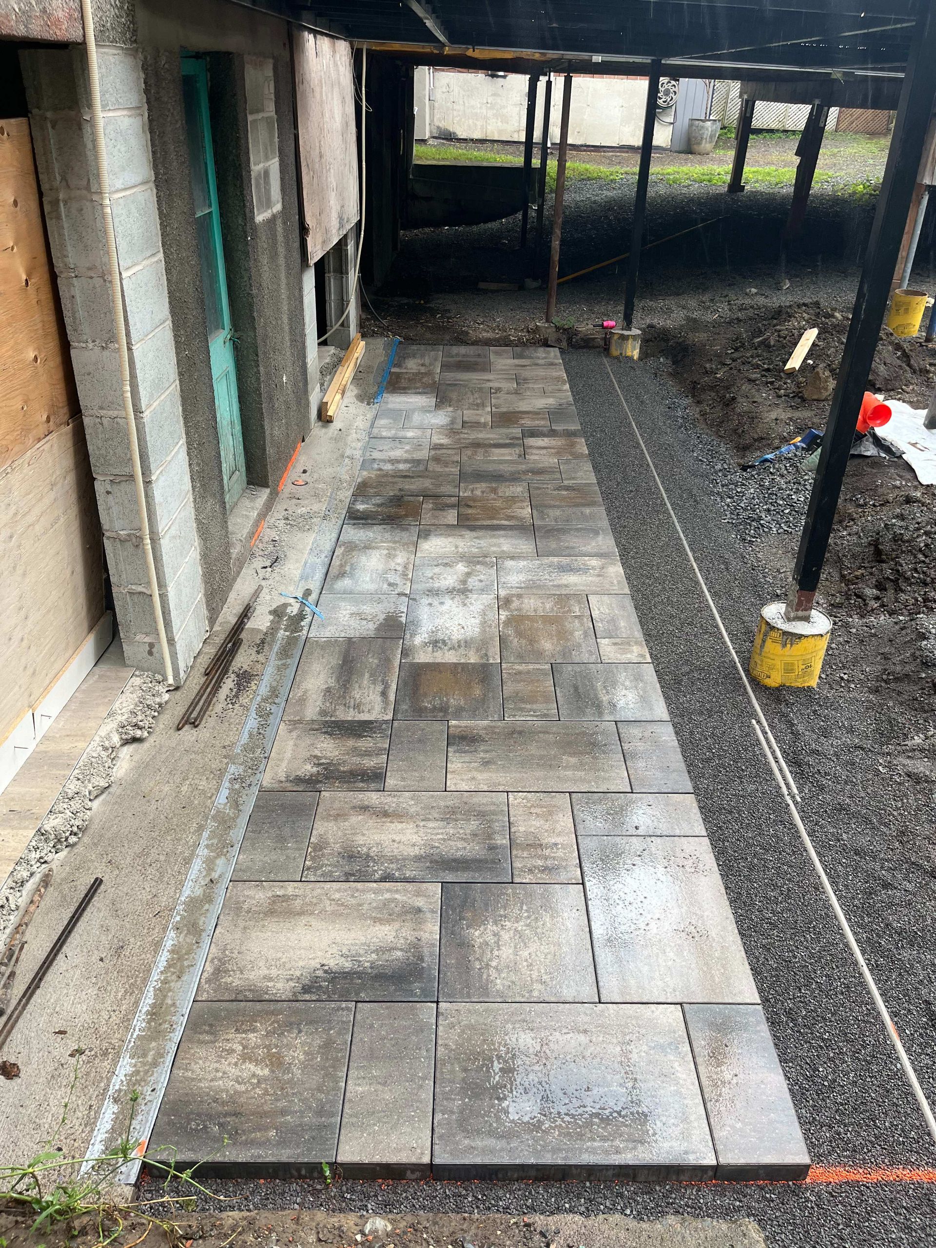 A stone walkway is being built in the backyard of a house.