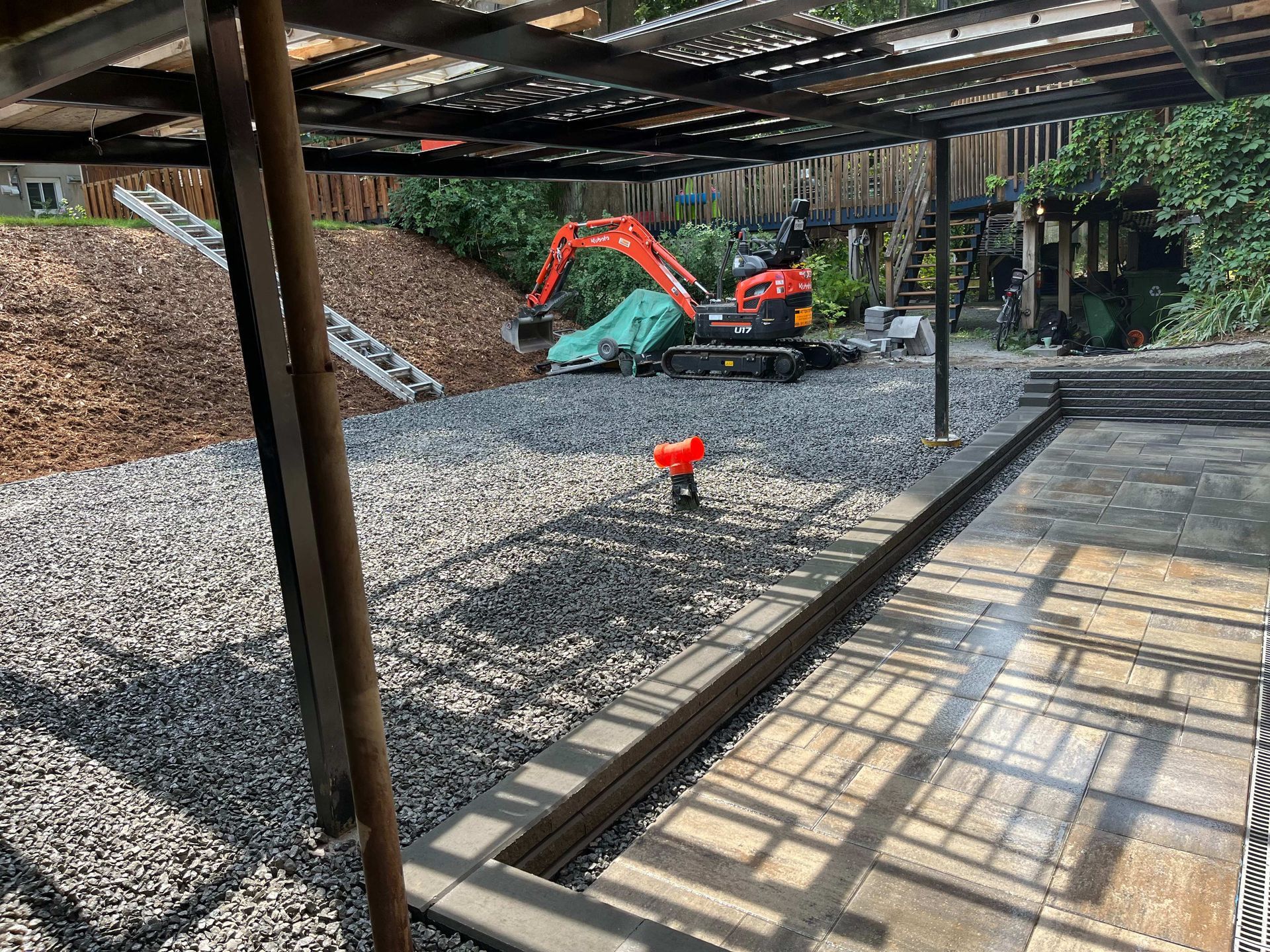 A small excavator is parked in a gravel yard under a covered area.