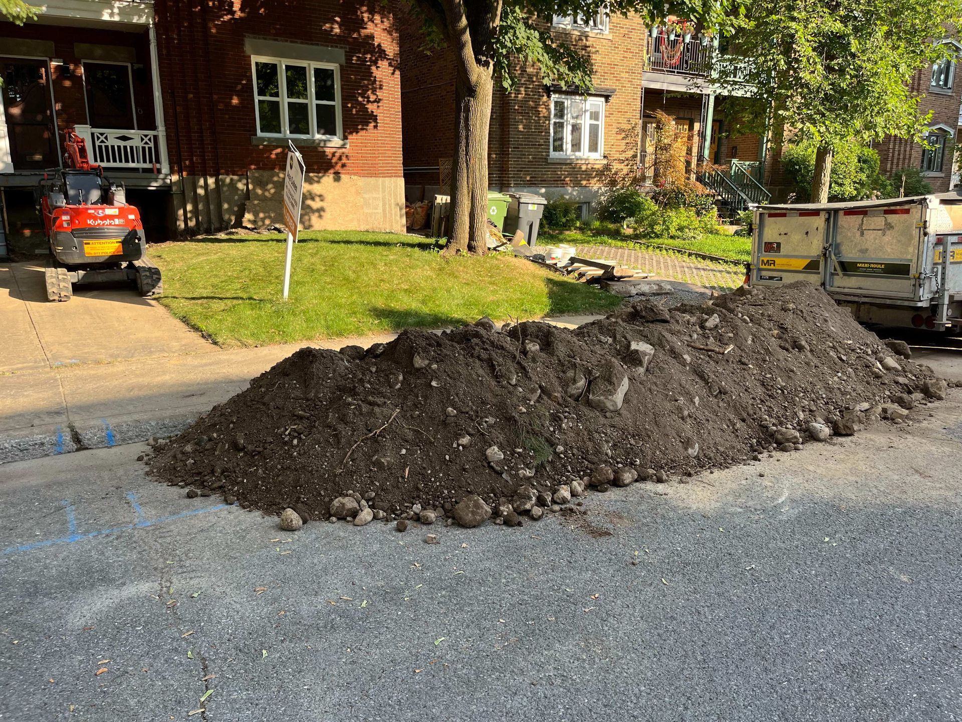 A pile of dirt is sitting on the side of the road in front of a house.
