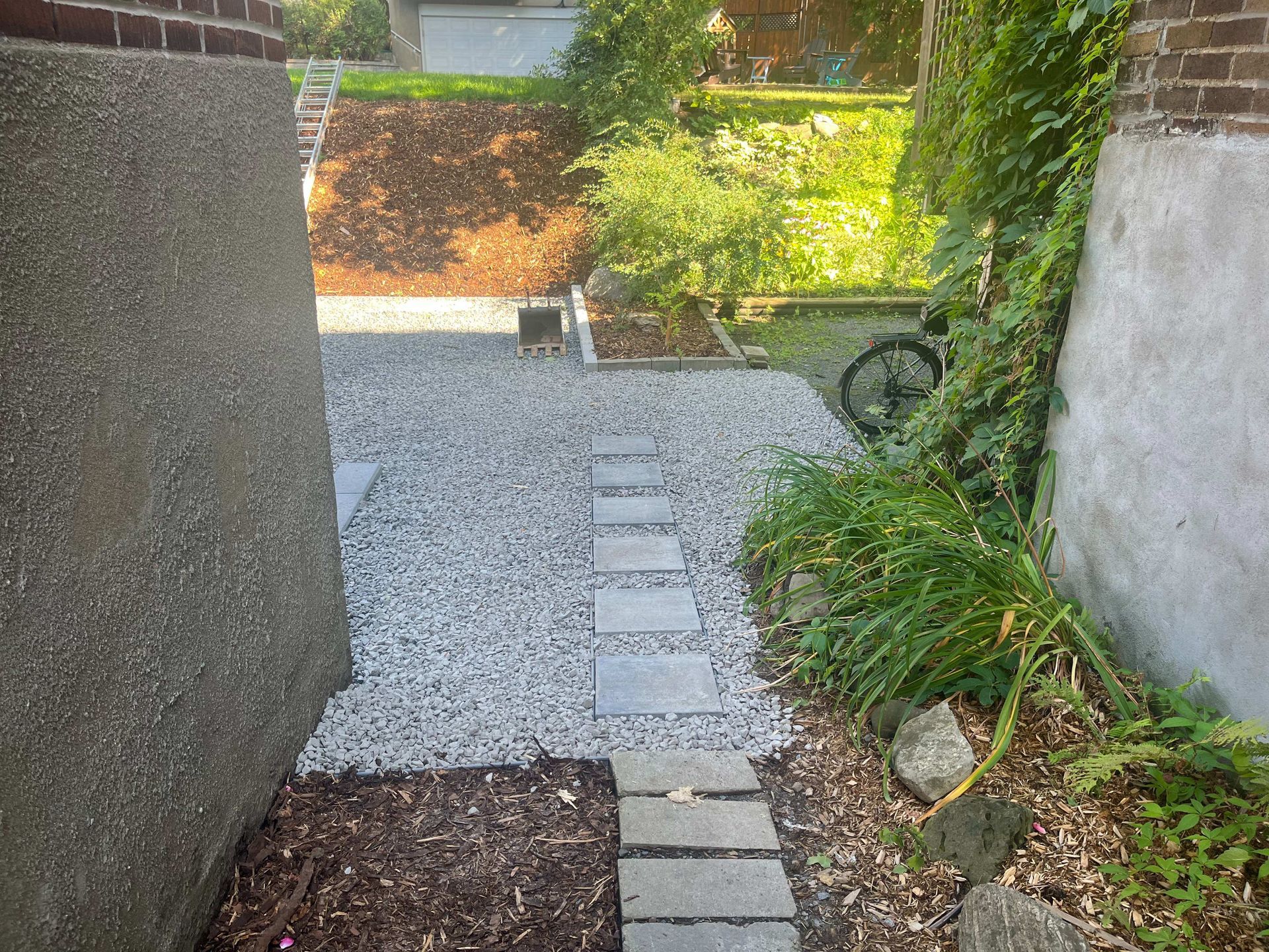 A stone walkway leading to a garden with a brick wall in the background.