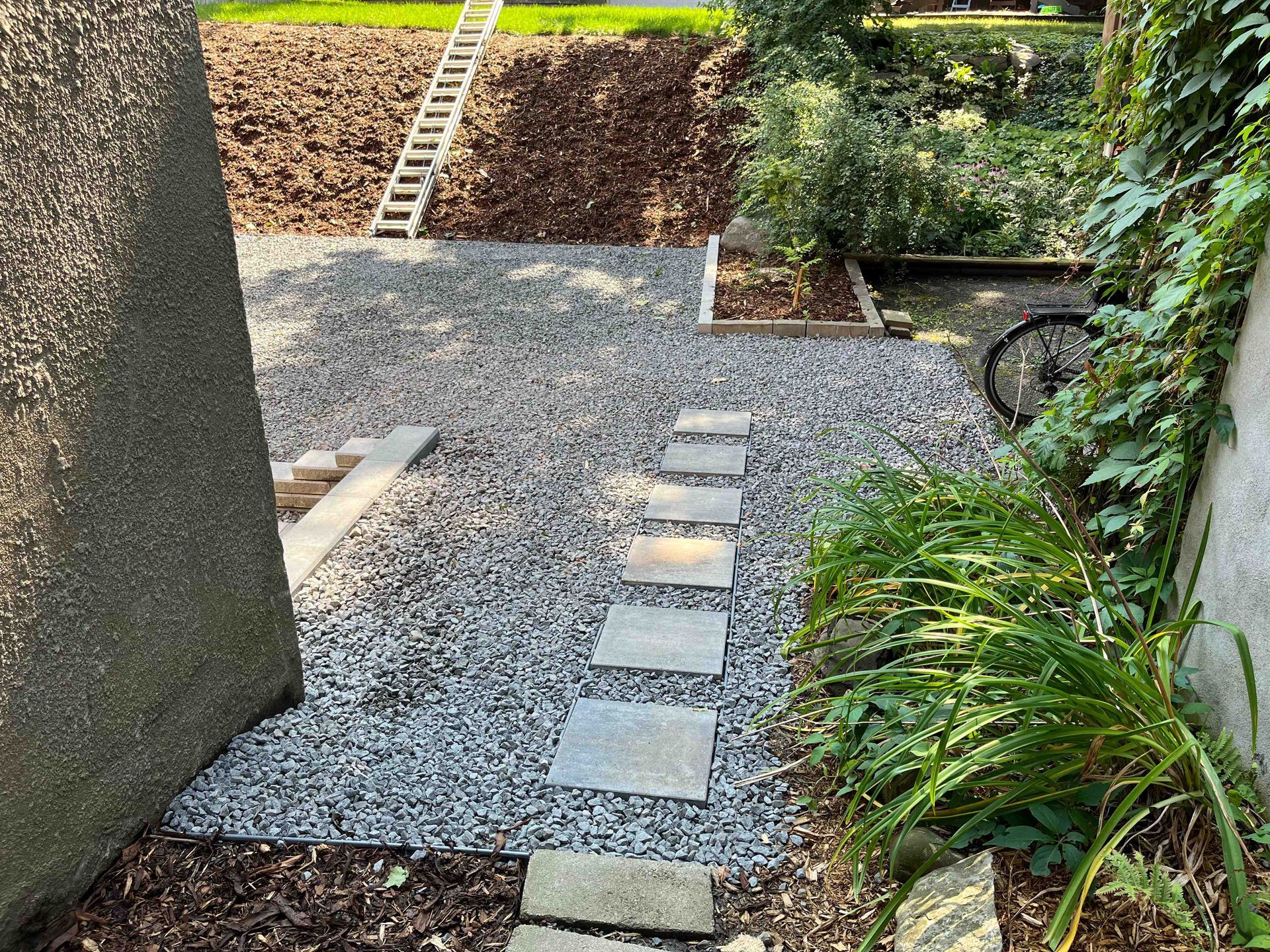 A stone walkway leading to a gravel area with a ladder in the background.