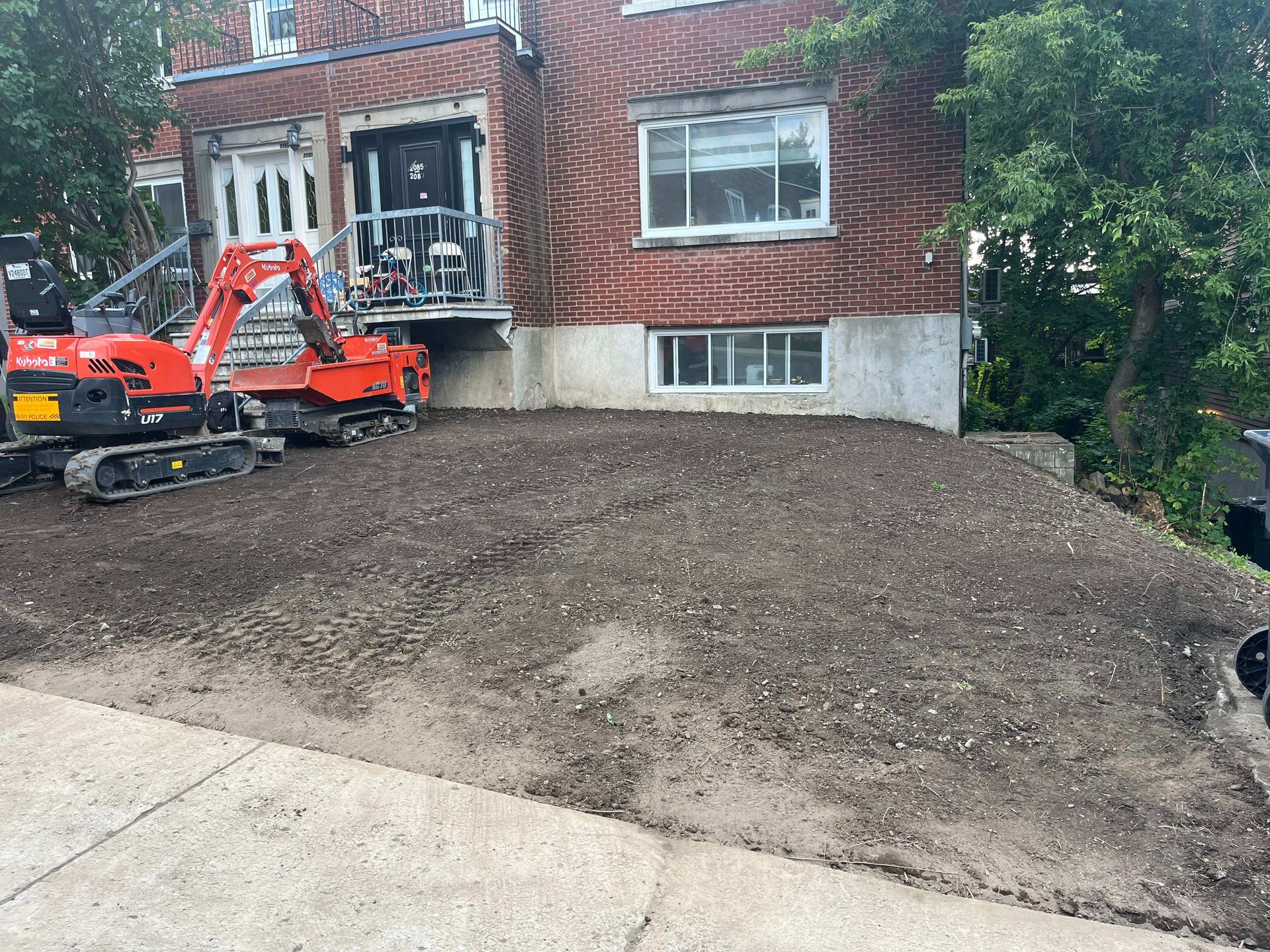 A red excavator is parked in front of a brick house