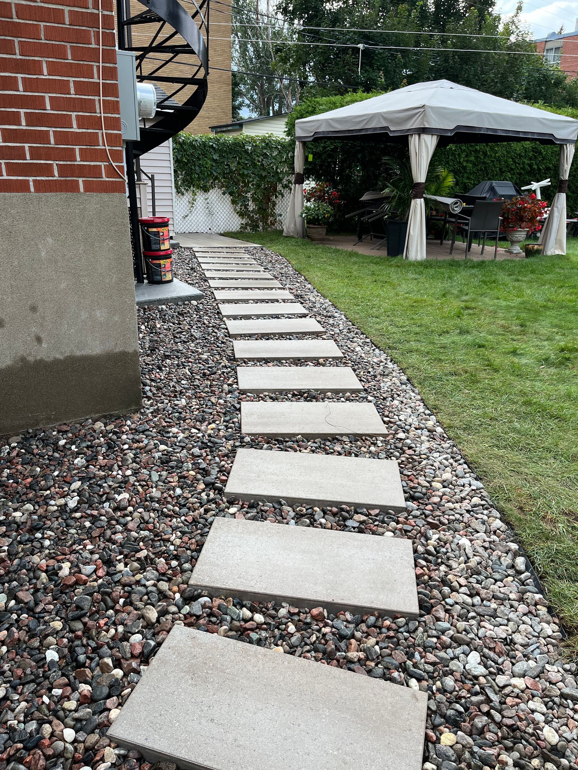 A stone walkway leading to a gazebo in a backyard.