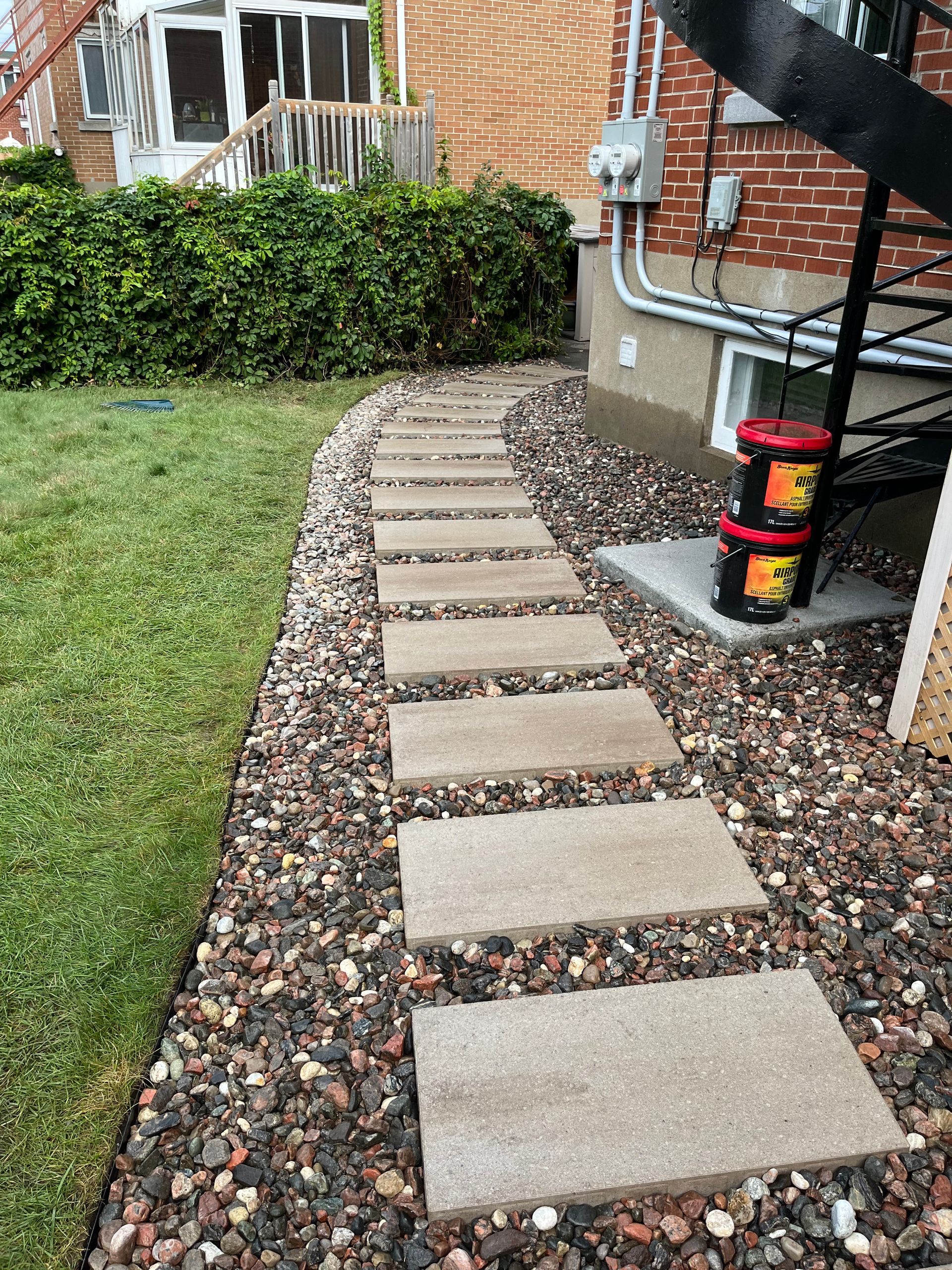A stone walkway leading to a house with buckets on the side of it.