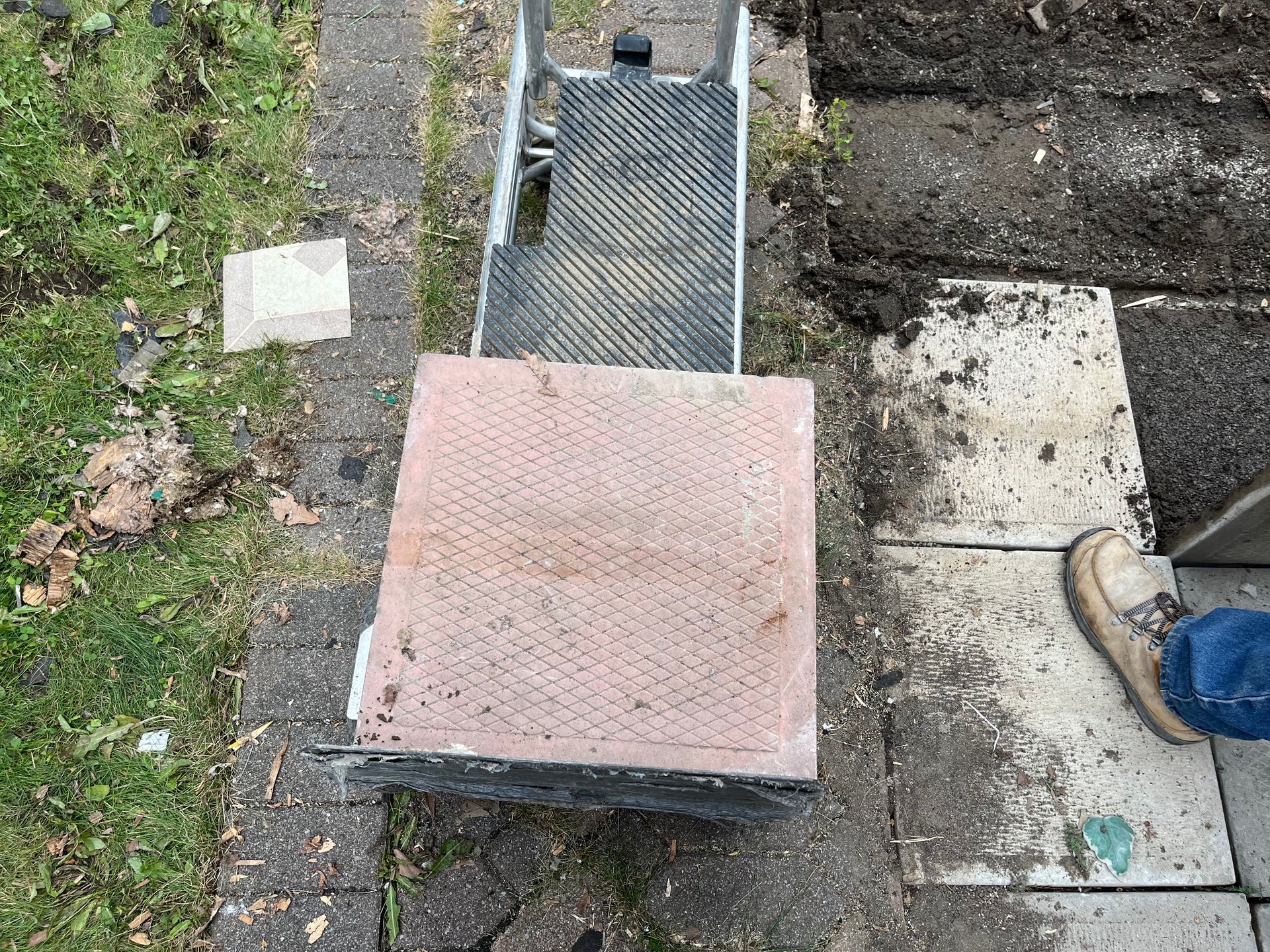 A person is laying bricks on a sidewalk next to a wheelbarrow.