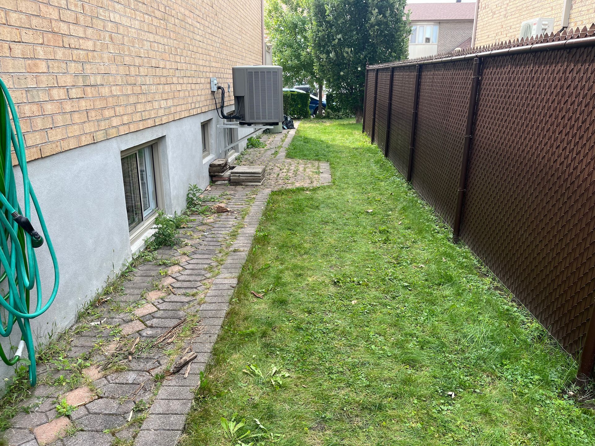 A hose is hanging on the side of a brick walkway next to a fence.