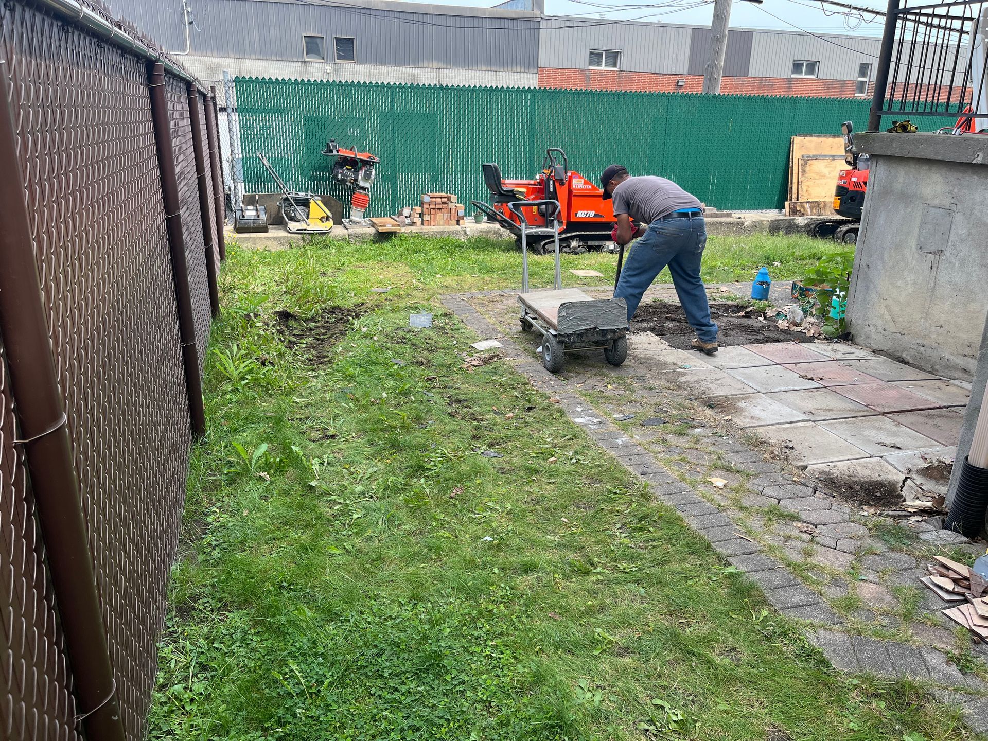 A man is working in a backyard with a wheelbarrow.