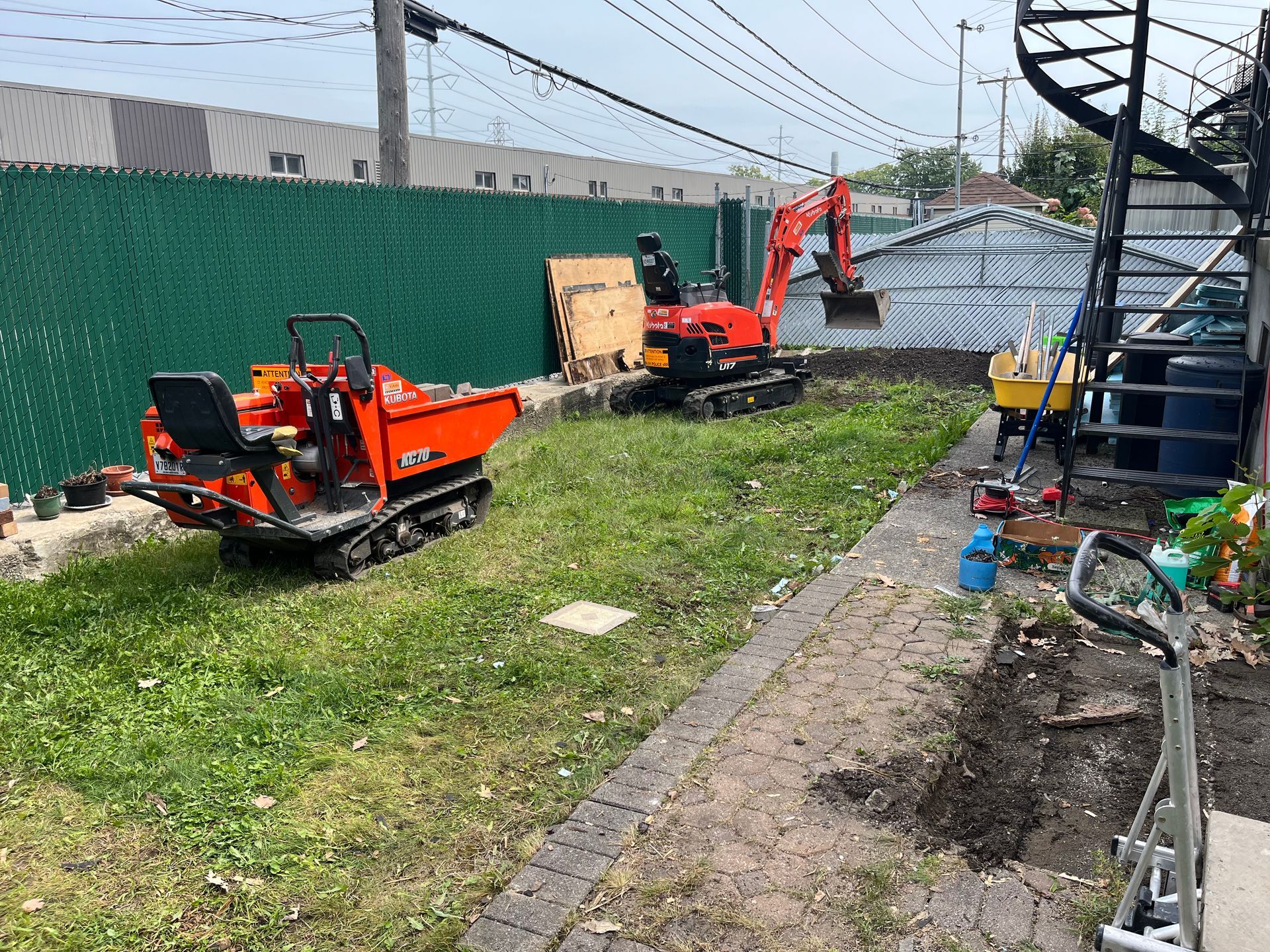 A small orange dump truck is parked in a grassy yard next to an excavator.