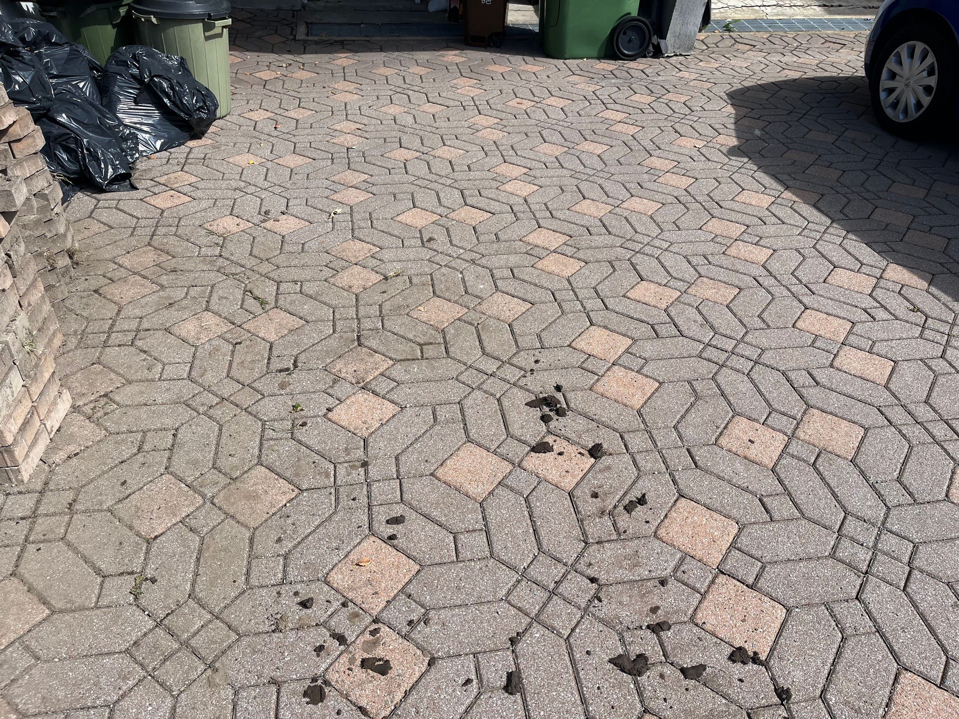 A brick driveway with a car parked in the background.
