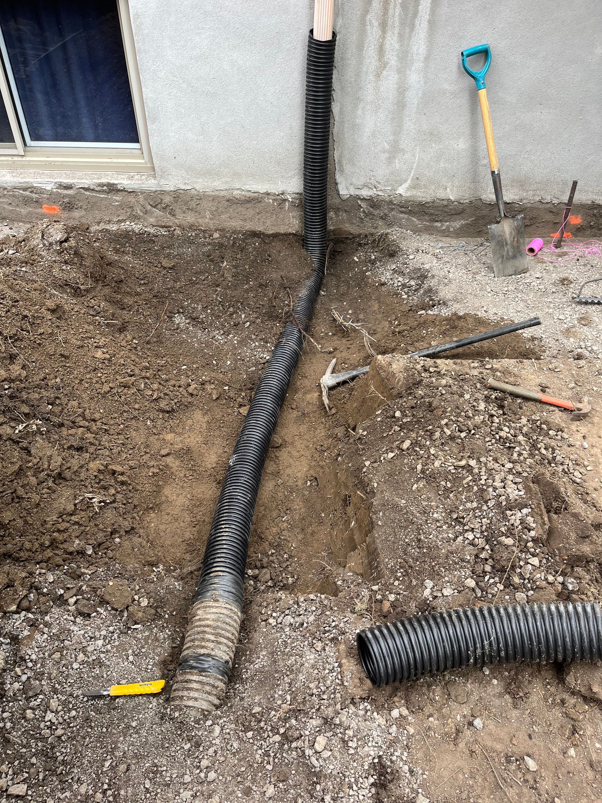 A drain pipe is being installed in the dirt next to a house.