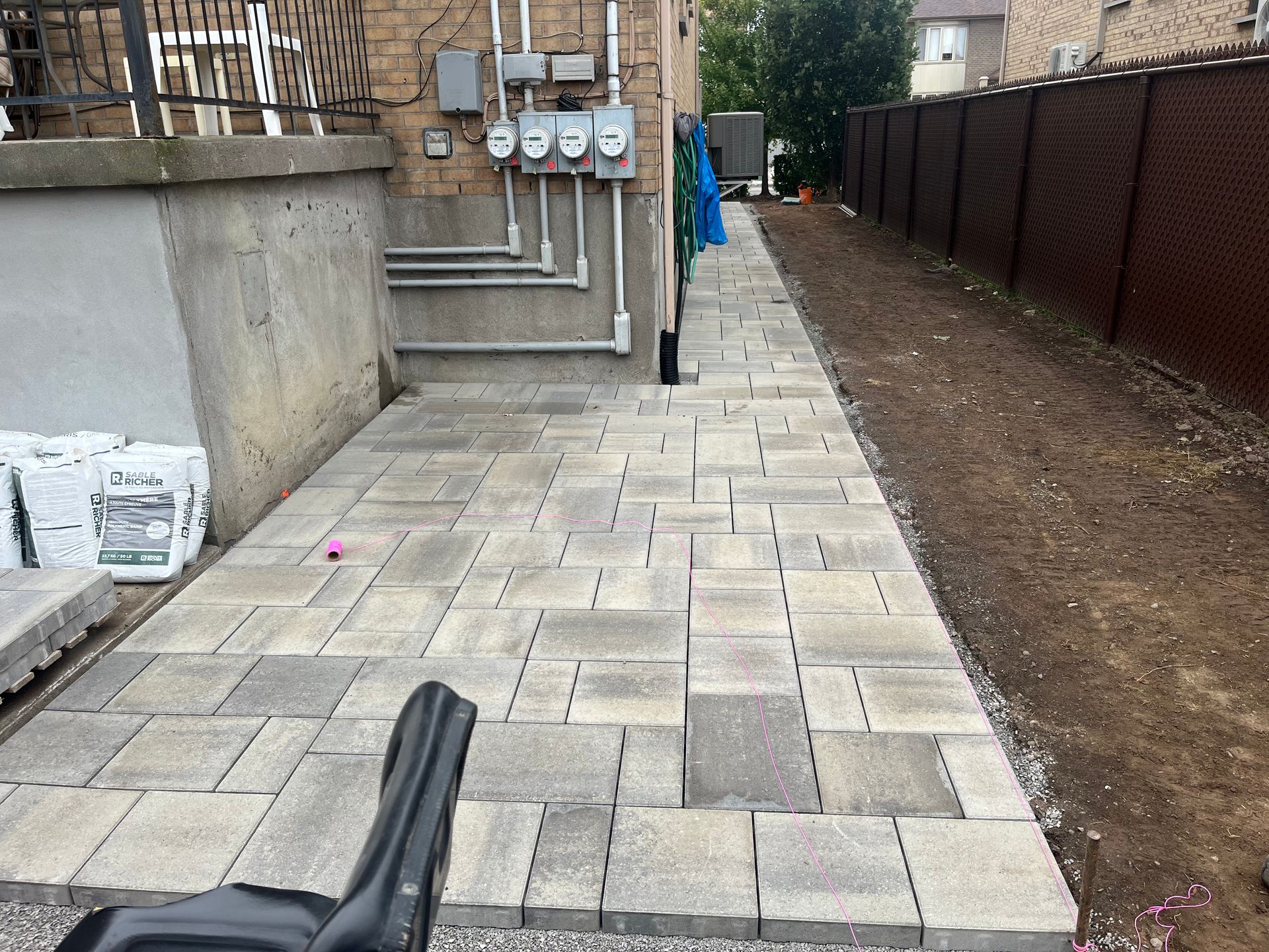 A brick walkway is being built in the backyard of a house