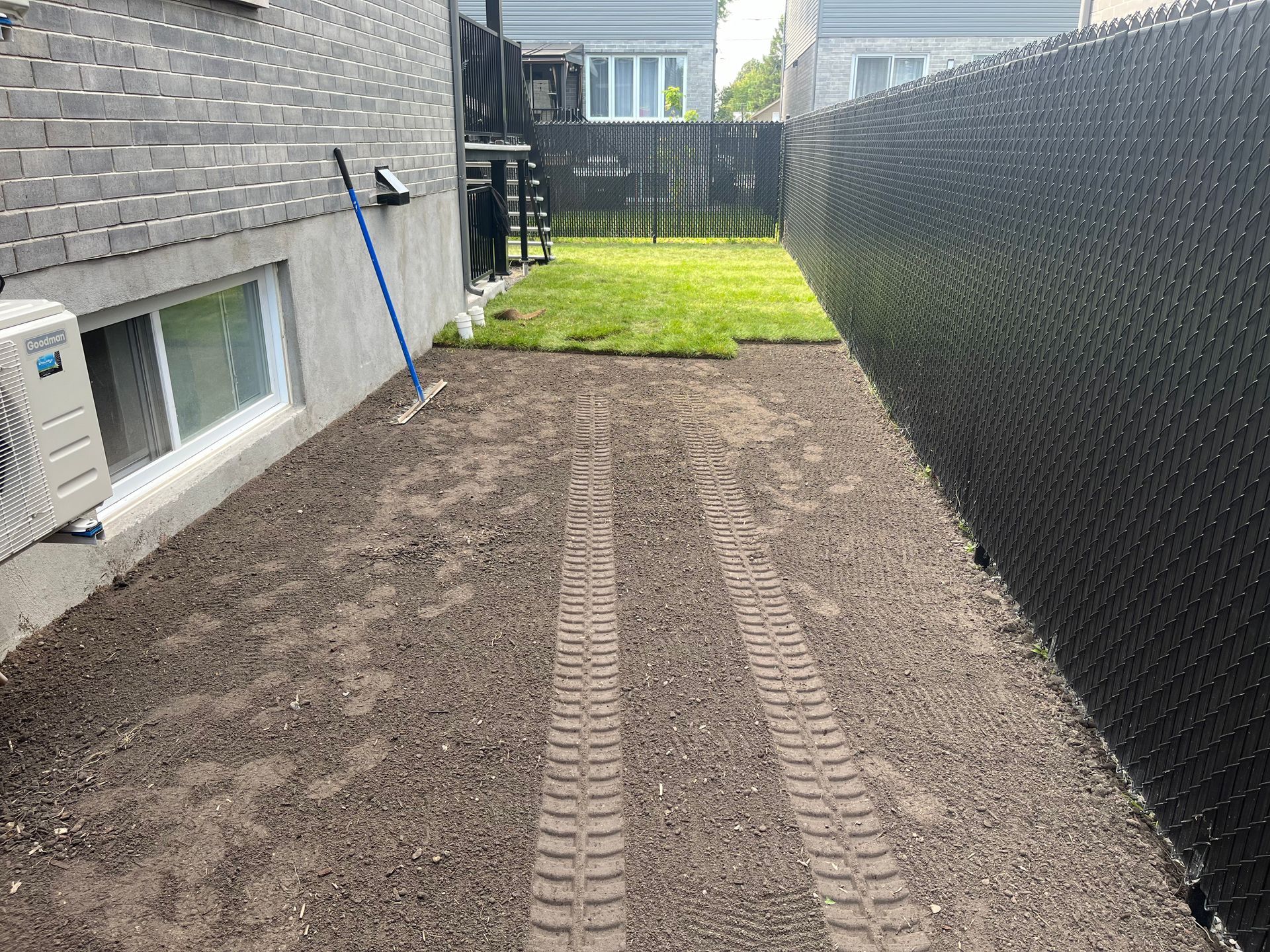 A backyard with a fence and a mop in the dirt.