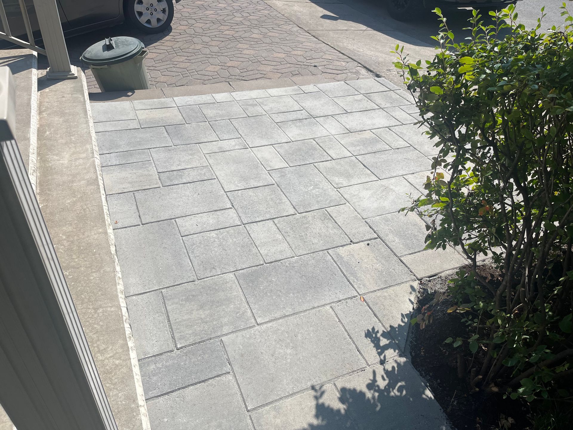 A sidewalk with a trash can and a car parked in the background.