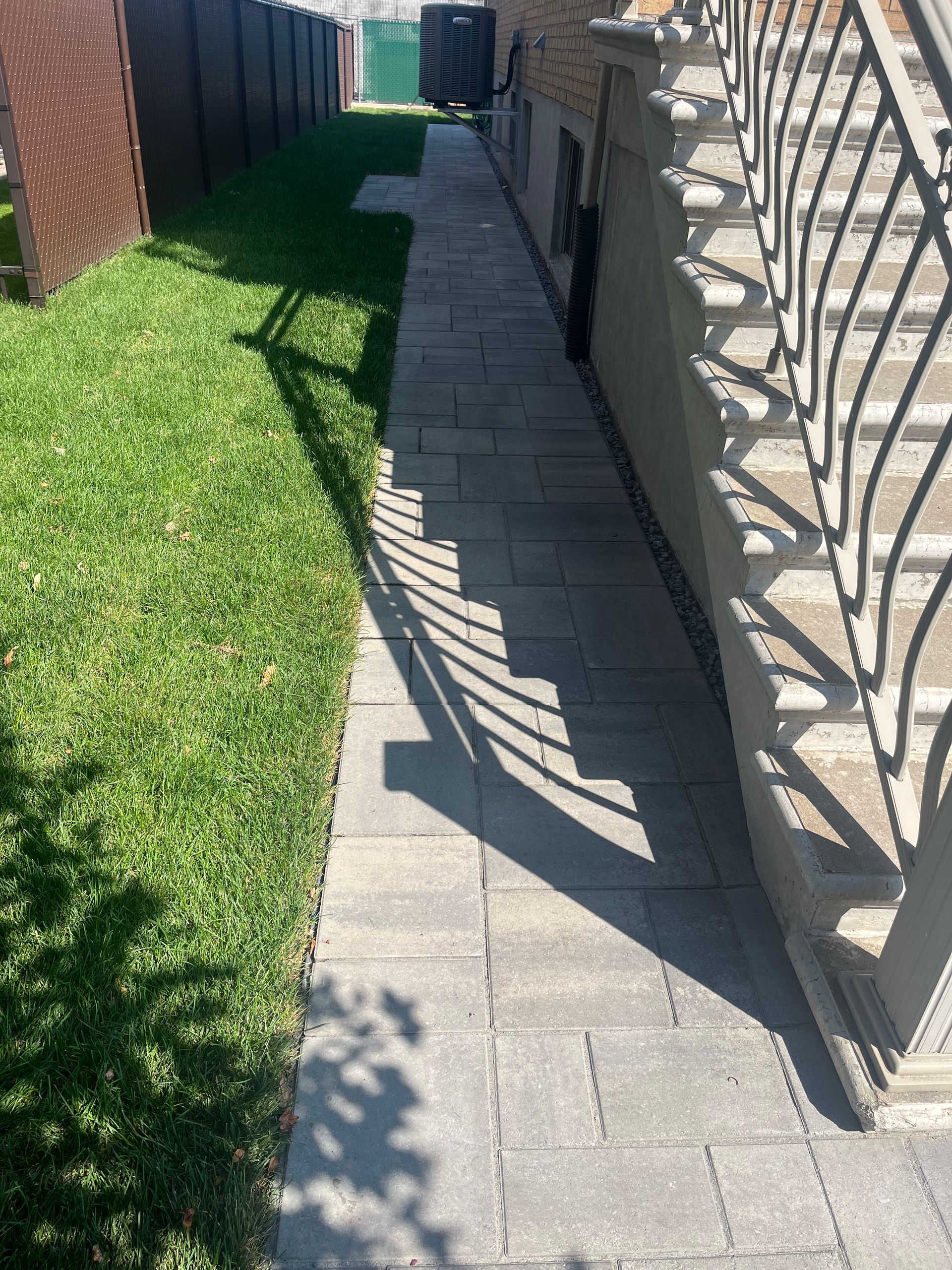 A sidewalk leading to a house with a wrought iron railing.
