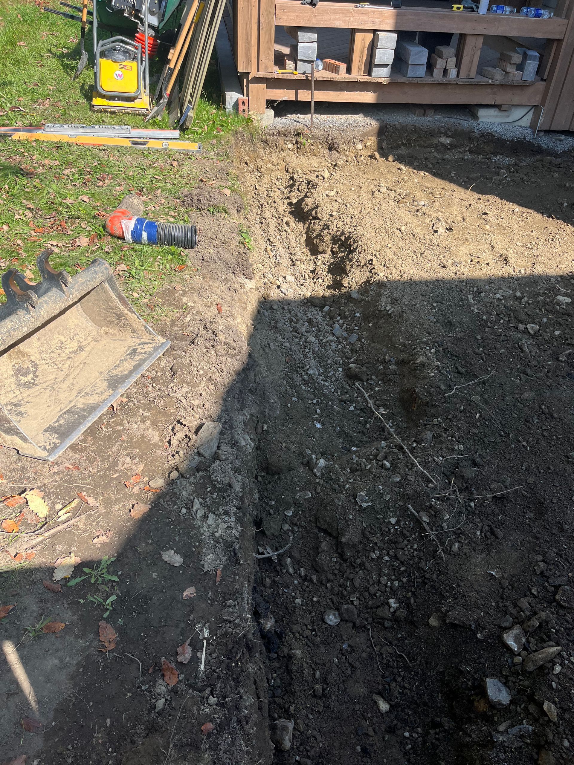 A shadow of a person is cast on a pile of dirt in a yard.