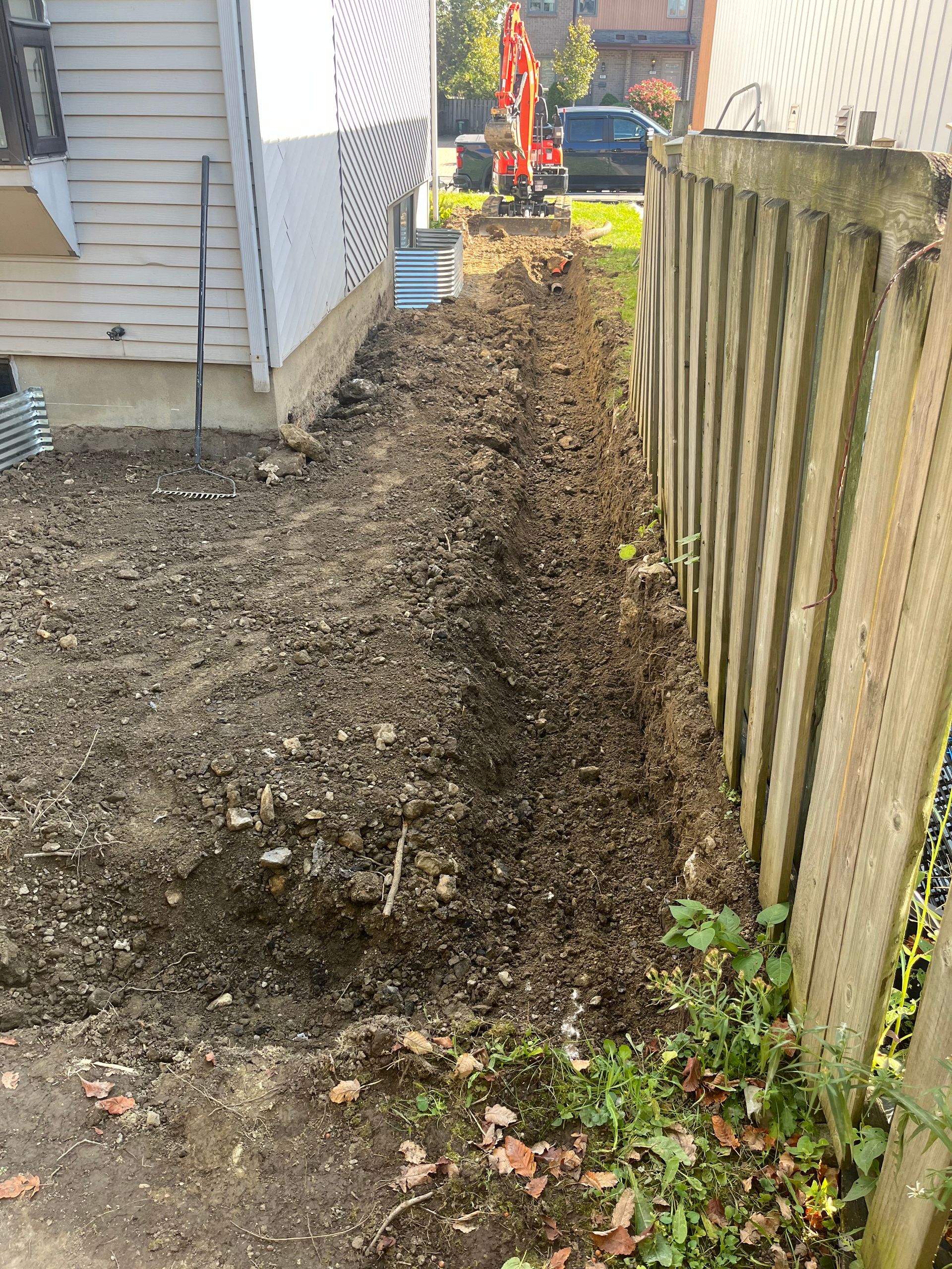 A large pile of dirt is next to a wooden fence and a house.