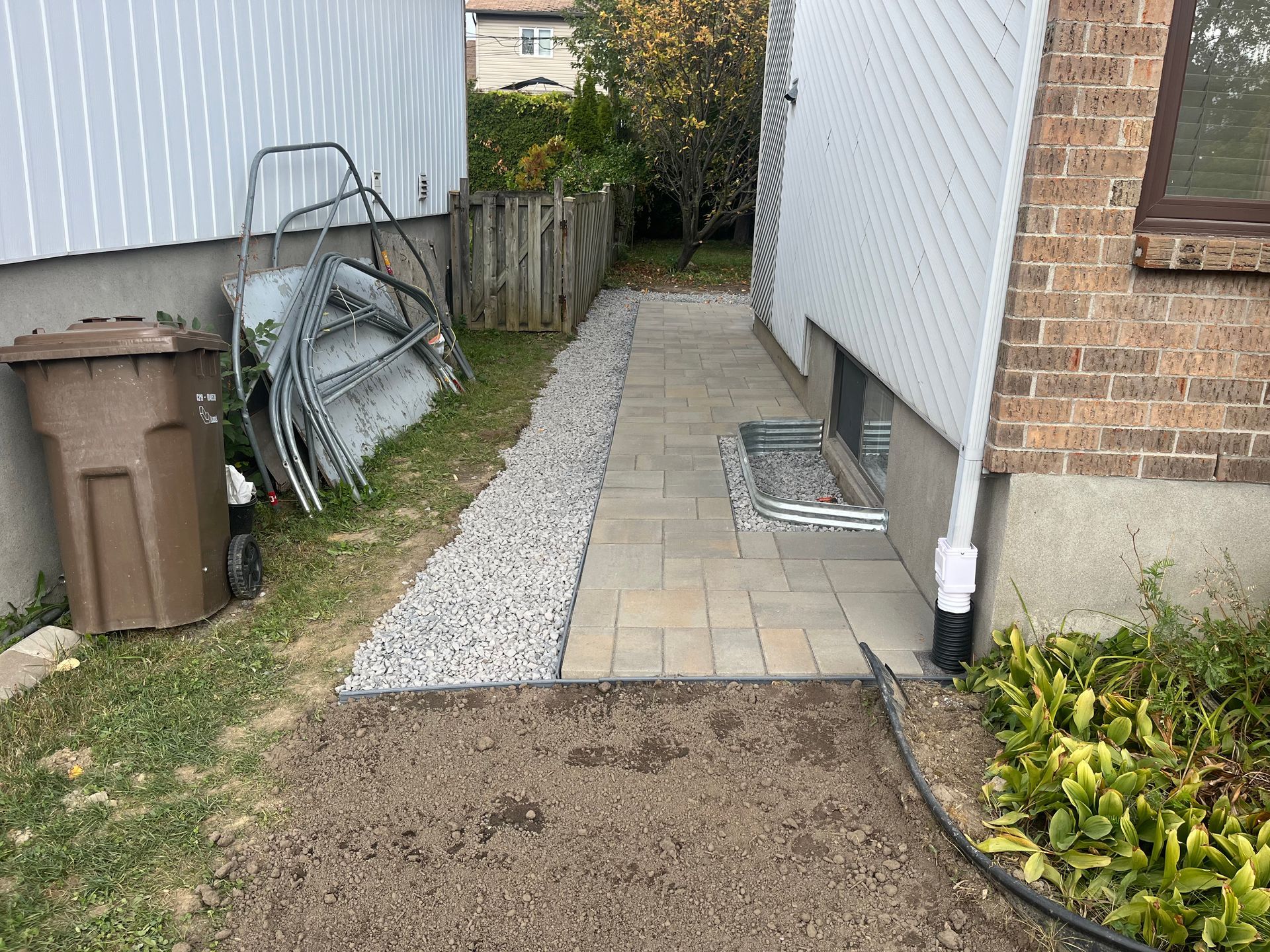 A sidewalk leading to a house with a trash can and a hose.